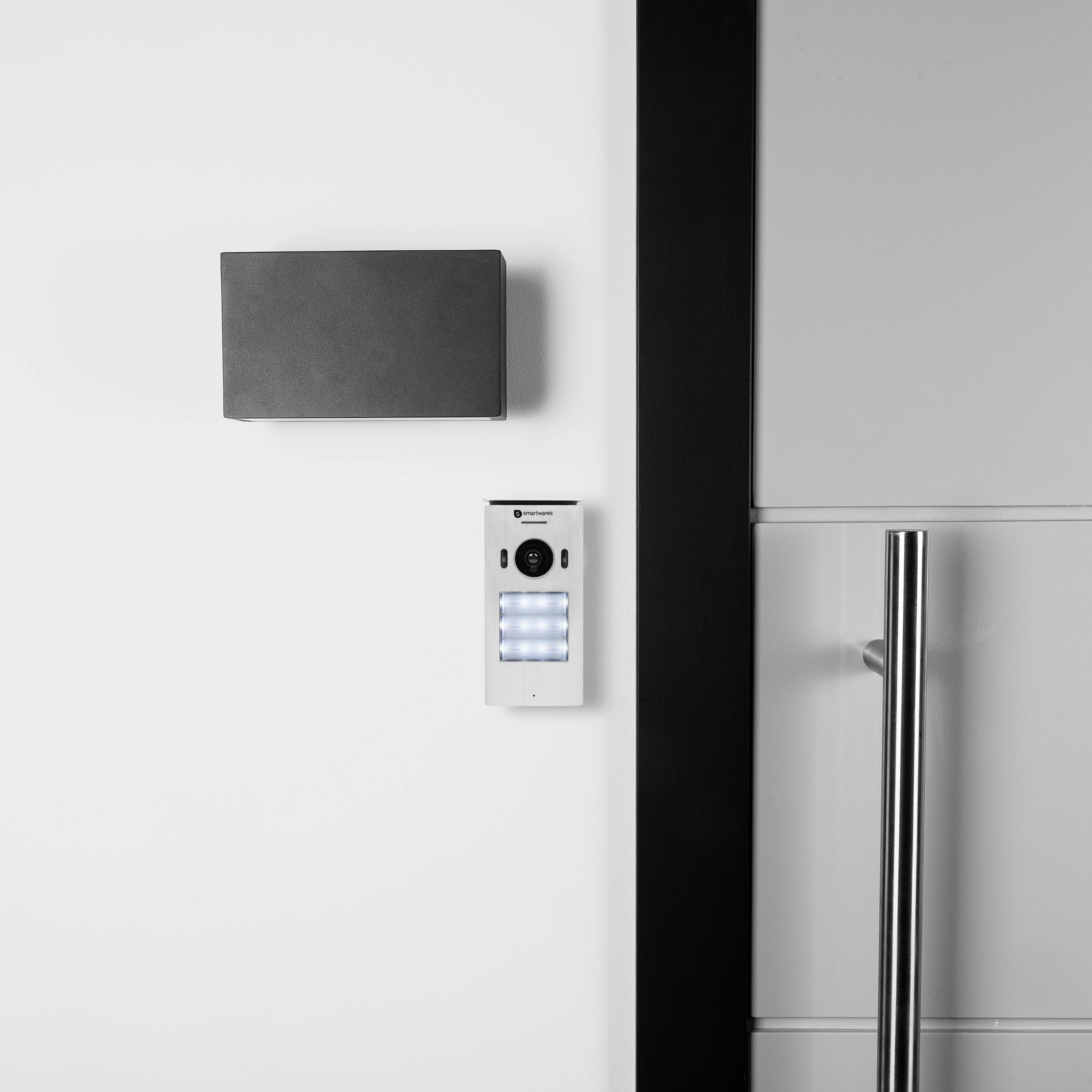 Zicht op een witte muur met een intercom naast een moderne deur met een metalen handvat, toont een beveiligingssysteem.