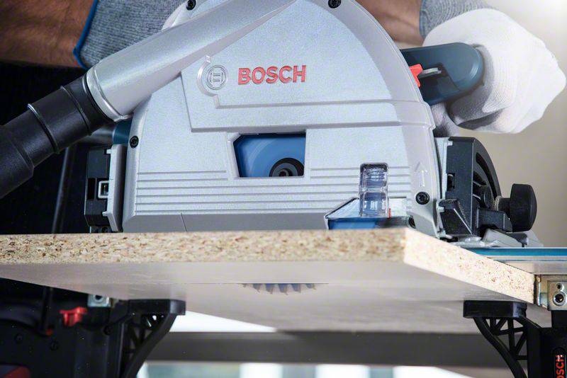 Een persoon zaagt een houten plaat met een Bosch-handcirkelzaag. De zaag heeft een stofzuigerslang voor het afzuigen van zaagsel.