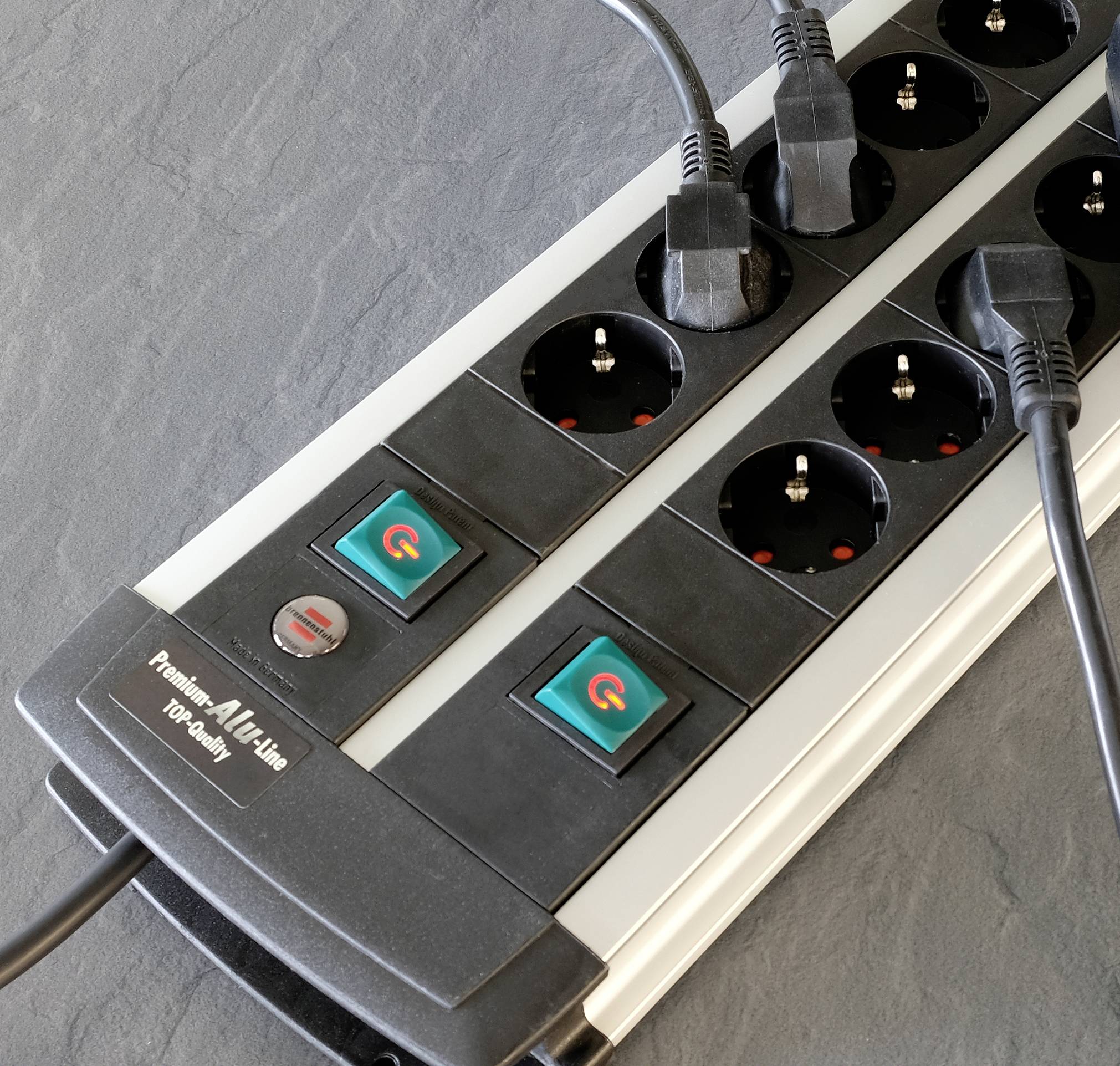 Zwarte stekkerdoos met vier stopcontacten en twee schakelaars op grijze achtergrond.