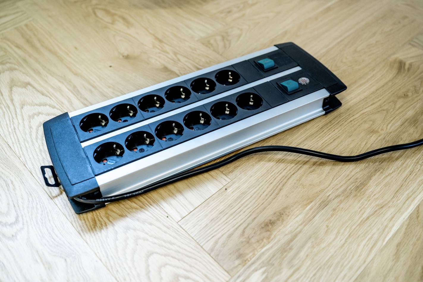 Een stekkerdoos met 12 stopcontacten en twee schakelaars ligt op een houten vloer.