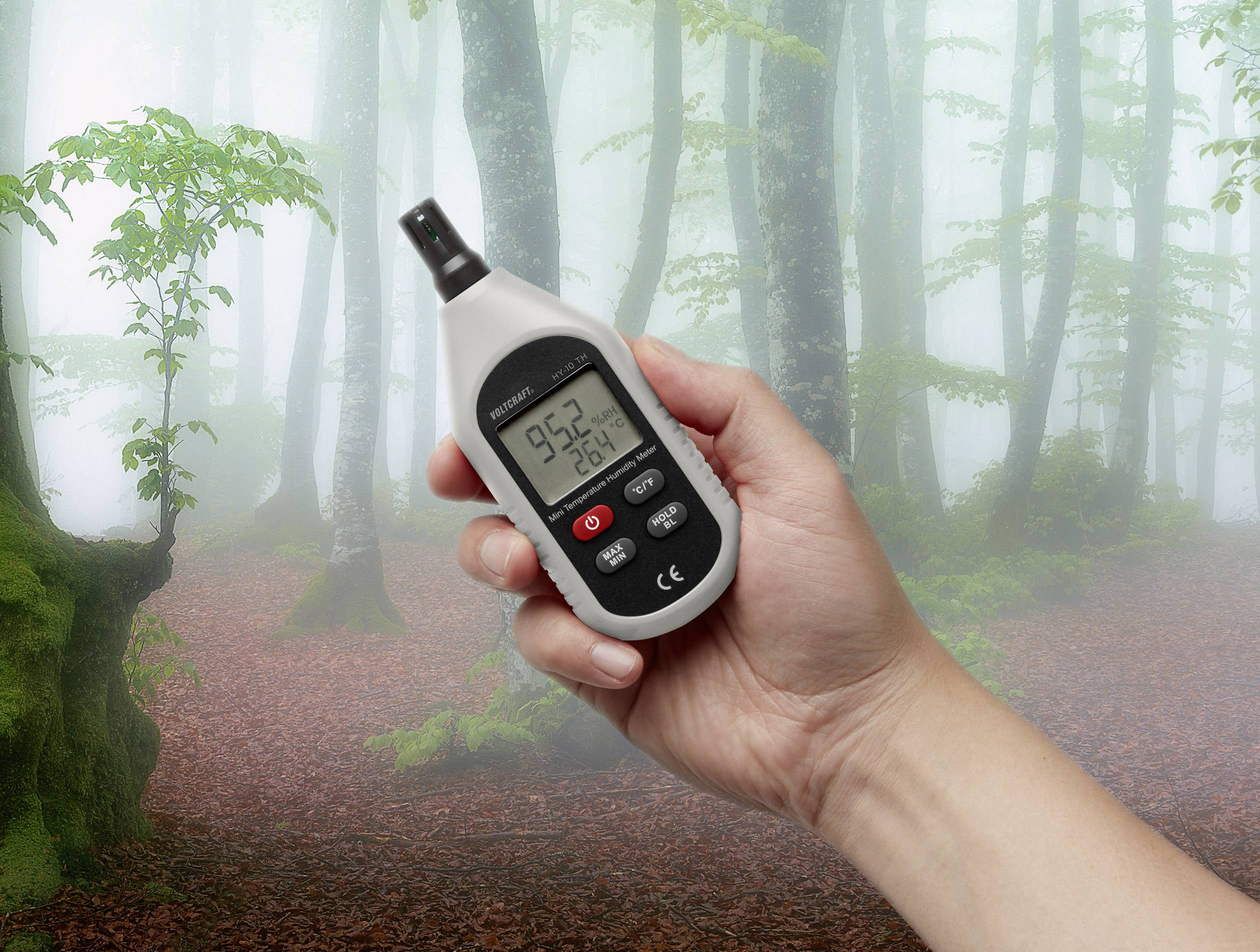 Een hand houdt een meetinstrument vast in een mistig bos. Display toont een temperatuur van 9,5 graden Celsius bij 76% luchtvochtigheid.