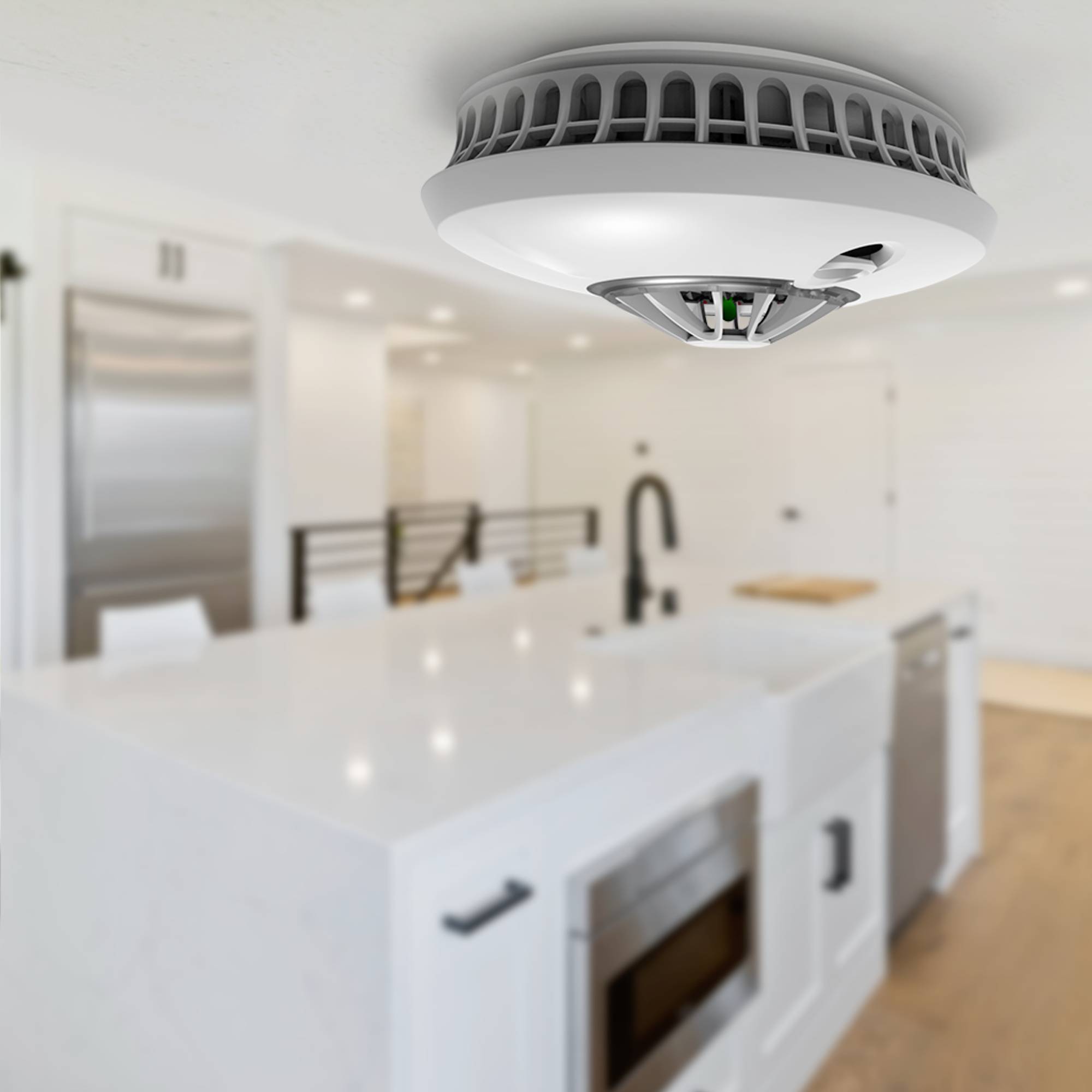Een rookmelder is geïnstalleerd aan het plafond van een moderne keuken. Op de achtergrond zijn witte keukenkastjes en een fornuis zichtbaar.