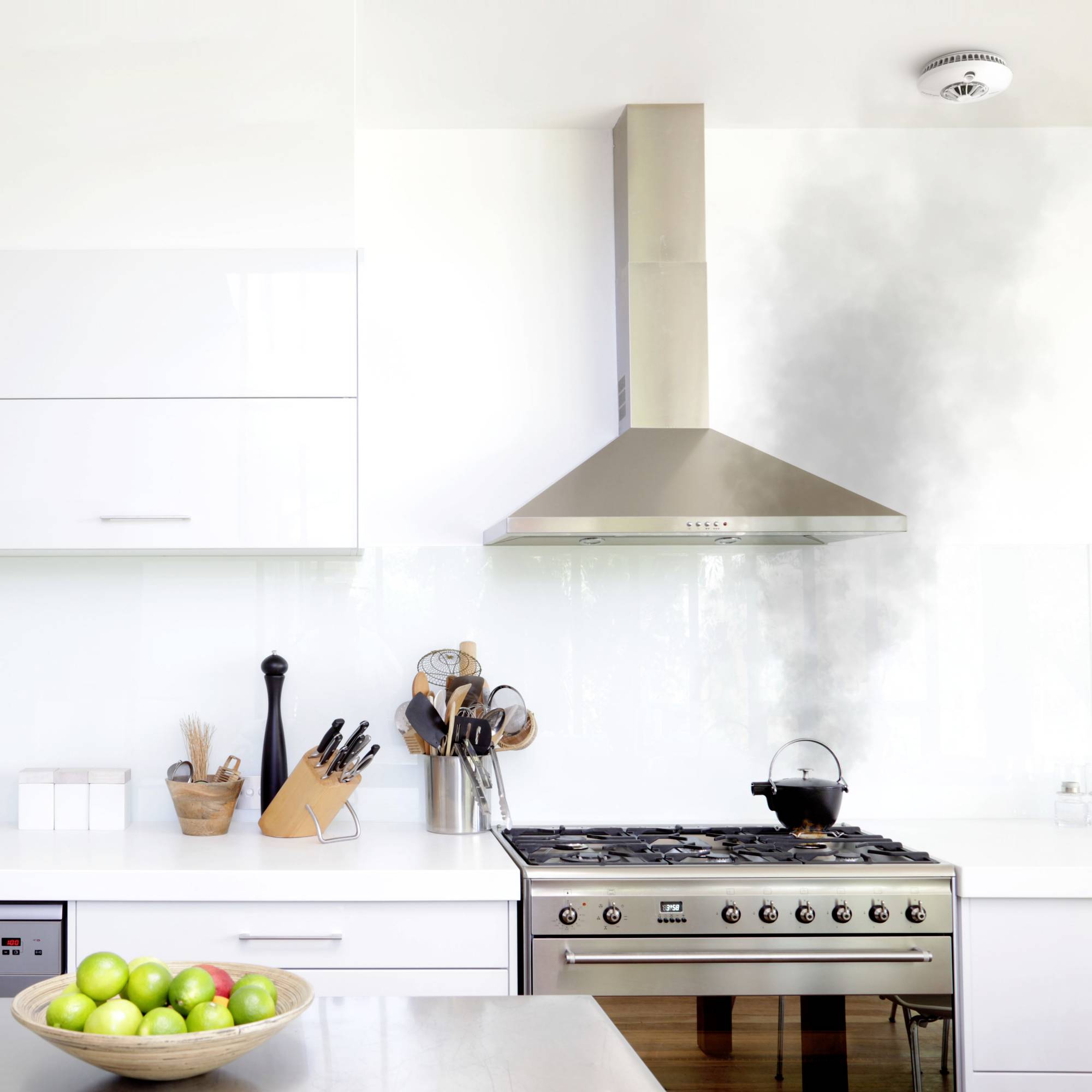 Keuken met een fornuis waarop een pan staat waaruit rook opstijgt. Een mand met appels op de voorgrond. Rookmelder aan het plafond.