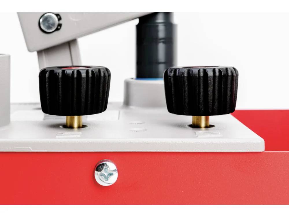 Close-upfoto van twee zwarte bedieningsknoppen op een rood en grijs apparaat, die een mechanisme aangeven voor het aanpassen of bedienen van machines.