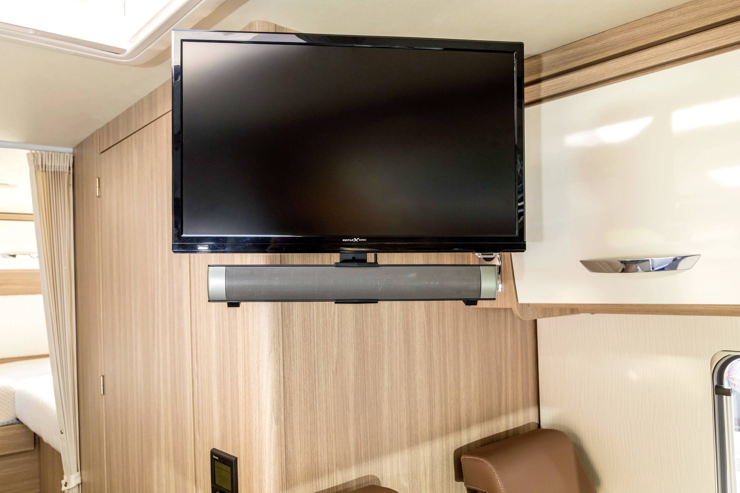 Een platte tv met luidsprekers is gemonteerd aan een houten beschoten wand, in een moderne woonruimte van een camper.
