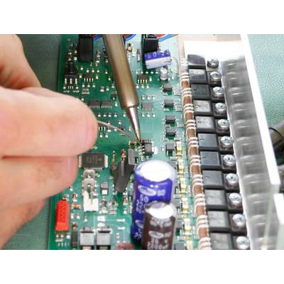 Een persoon soldeert componenten op een groene printplaat die is uitgerust met verschillende elektronische onderdelen.