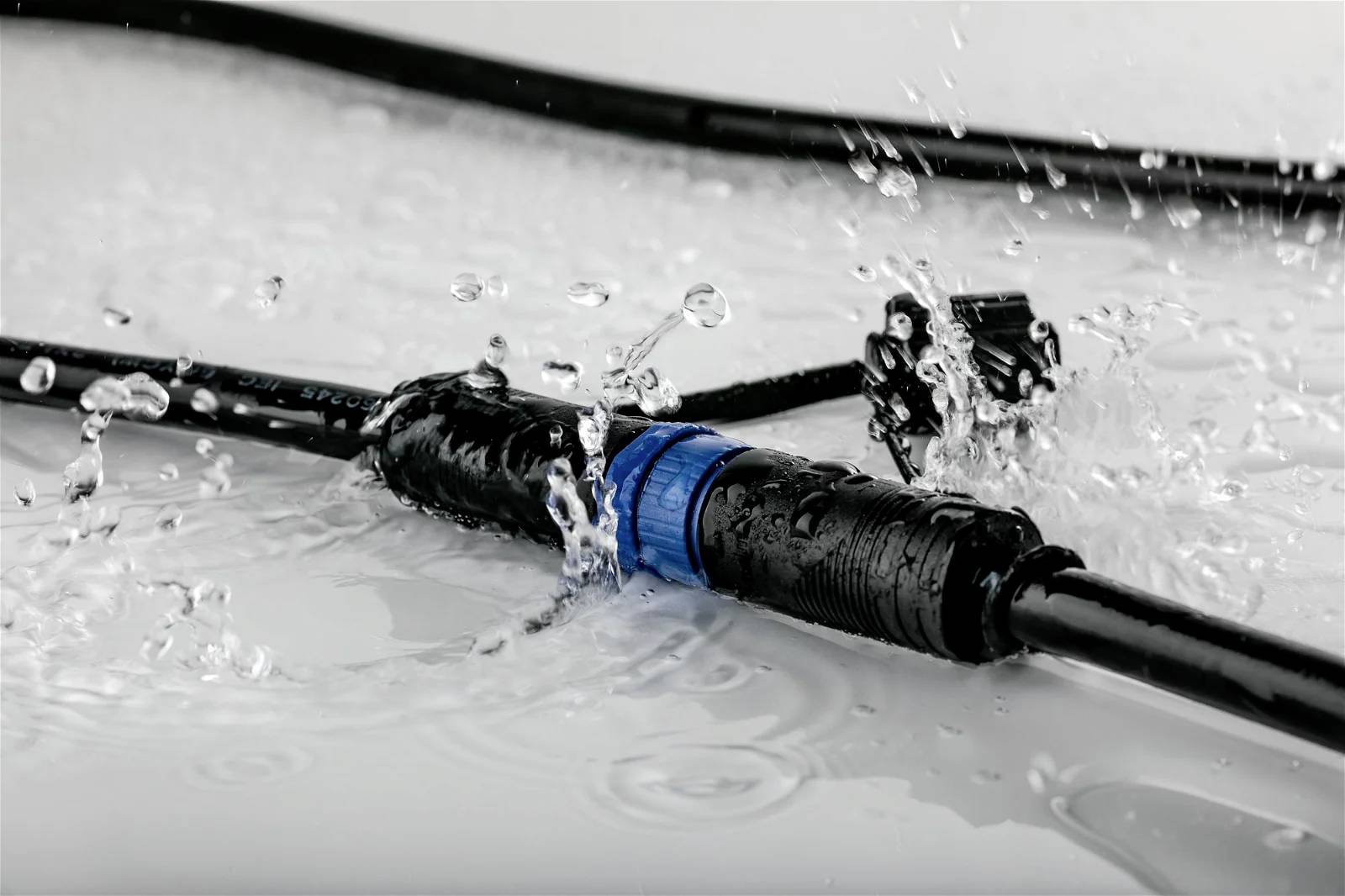 Een waterdichte elektrische stekker spat water op een gladde oppervlakte. Kabels zijn aangesloten en zichtbaar op de voorgrond.