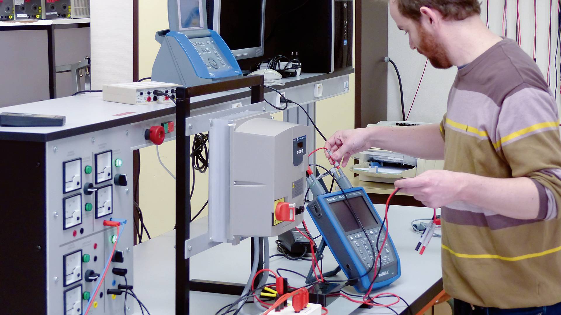 Een man werkt geconcentreerd aan een elektronische laboratoriumtafel met meetapparatuur en kabels.