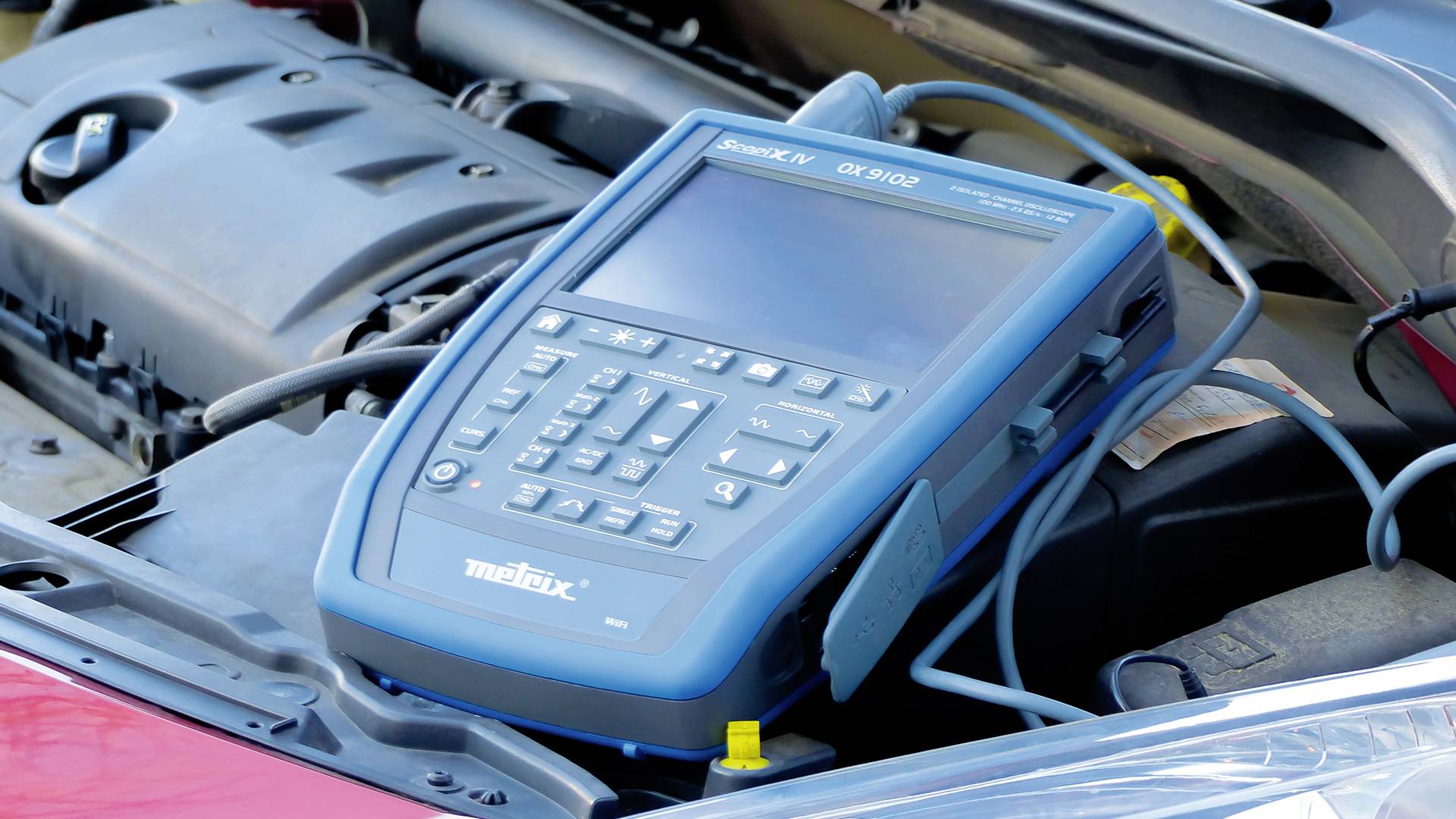 Een diagnoserapport is aangesloten in de motorruimte van een auto om voertuiggegevens uit te lezen en mogelijke problemen te identificeren.