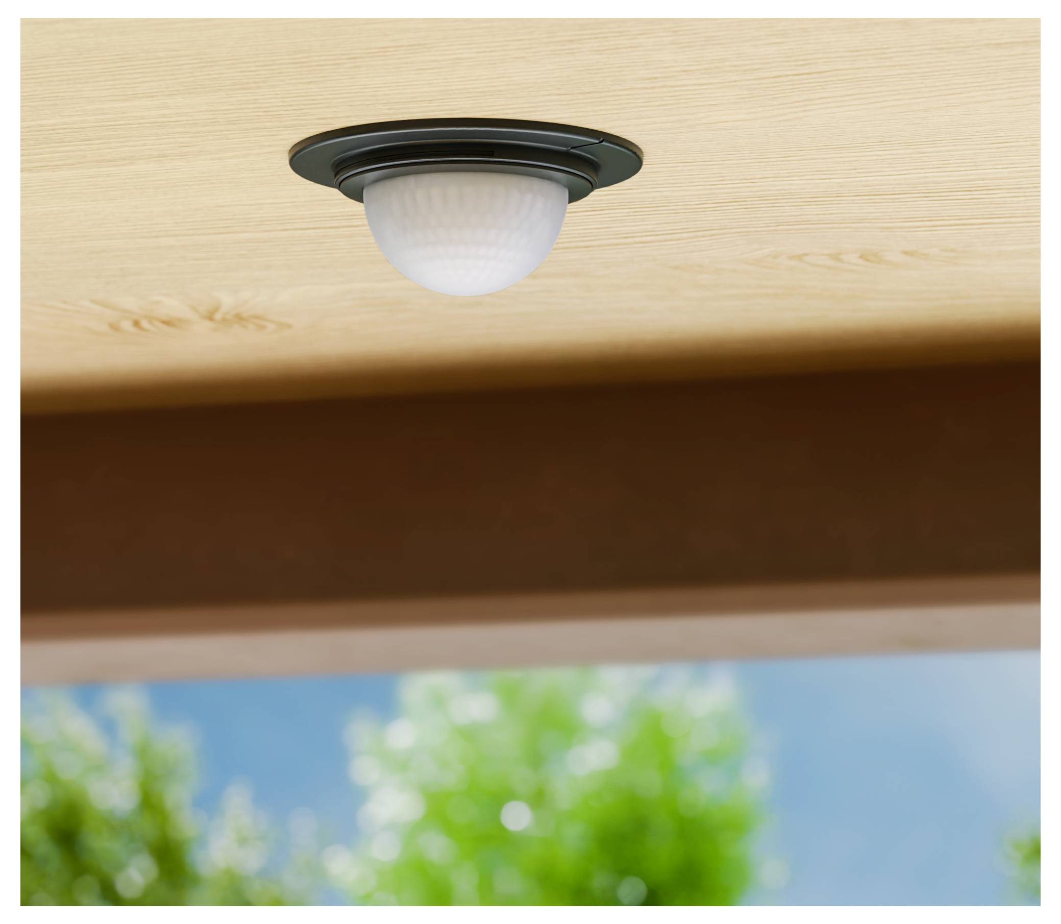 Een inbouwplafondlamp met matglas is op een houten plafond geïnstalleerd, met een onscherp buitenlandschap eronder.