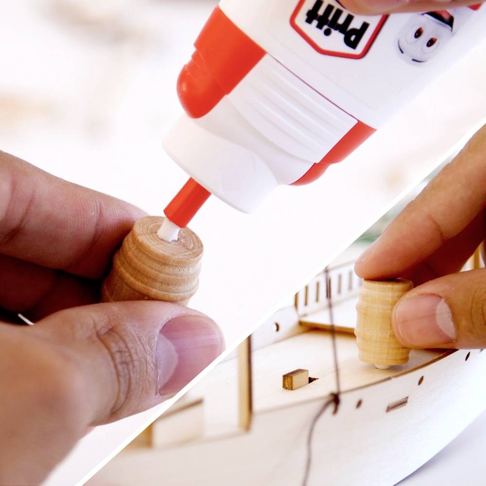 Een persoon die lijm aanbrengt op een klein houten onderdeel, terwijl hij een modelboot in elkaar zet; symboliseert precisie en vakmanschap.