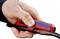 Een hand houdt een Knipex-gereedschap vast dat een kabel ontmantelt. Het gereedschap is rood met een blauwe opdruk van de merknaam.