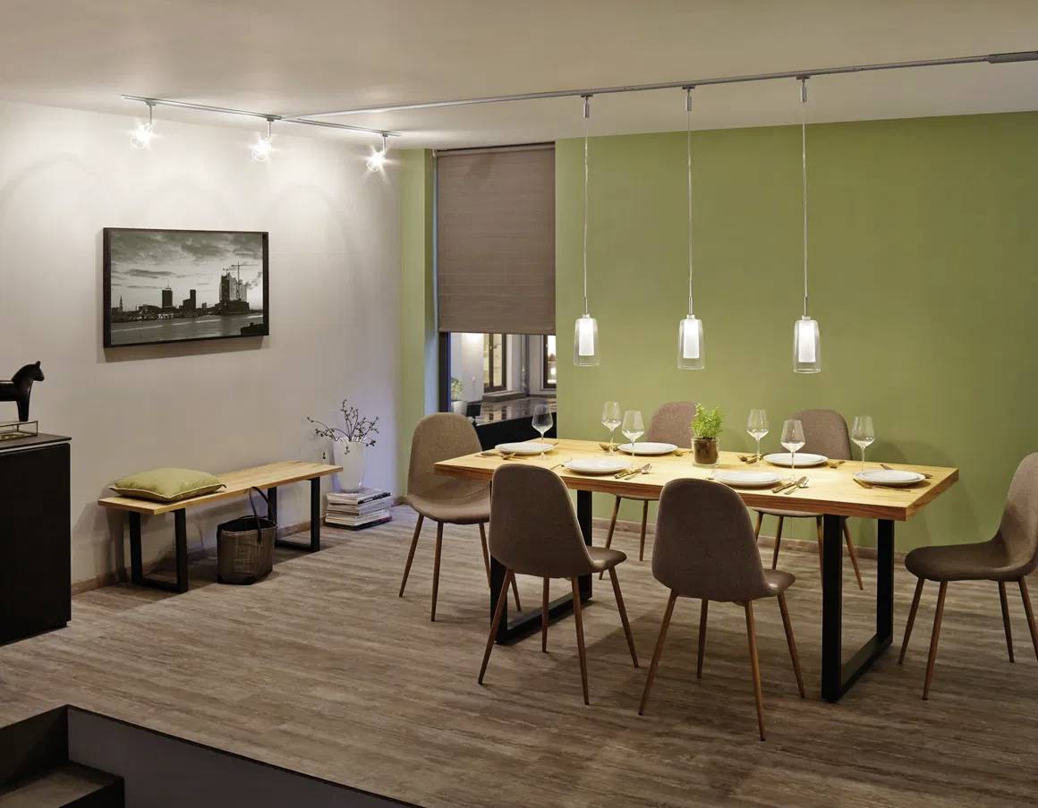 Moderne open keuken met barkrukken, een gezellige bank en fauteuils in een licht verlichte ruimte. Grote ramen met zicht naar buiten.