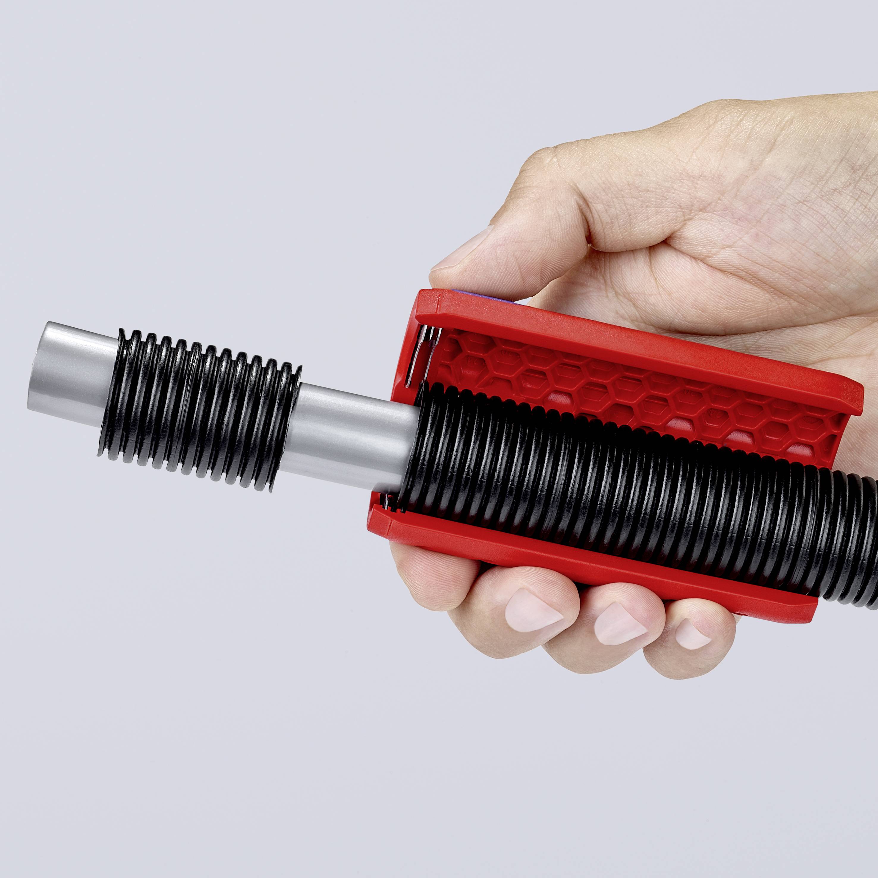 Hand houdt een rood gereedschap met een zwarte spiraalveer vast op een grijze achtergrond.