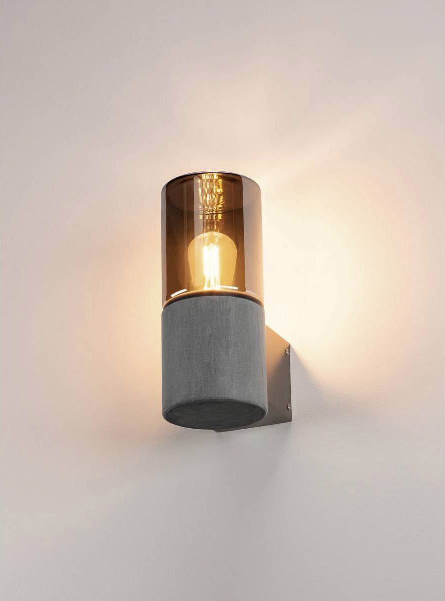 Wandlamp met cilindrische glazen kap en zichtbare lichtbron verspreidt warm licht op een witte muur.