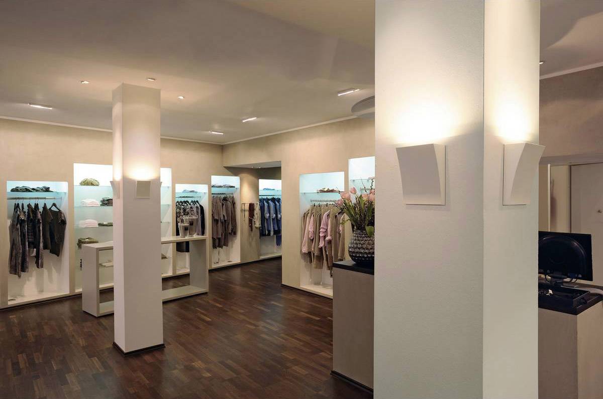 Moderne kledingwinkel met houten vloer, verlichte schappen met kleding en accessoires, zacht licht, uitnodigende sfeer.