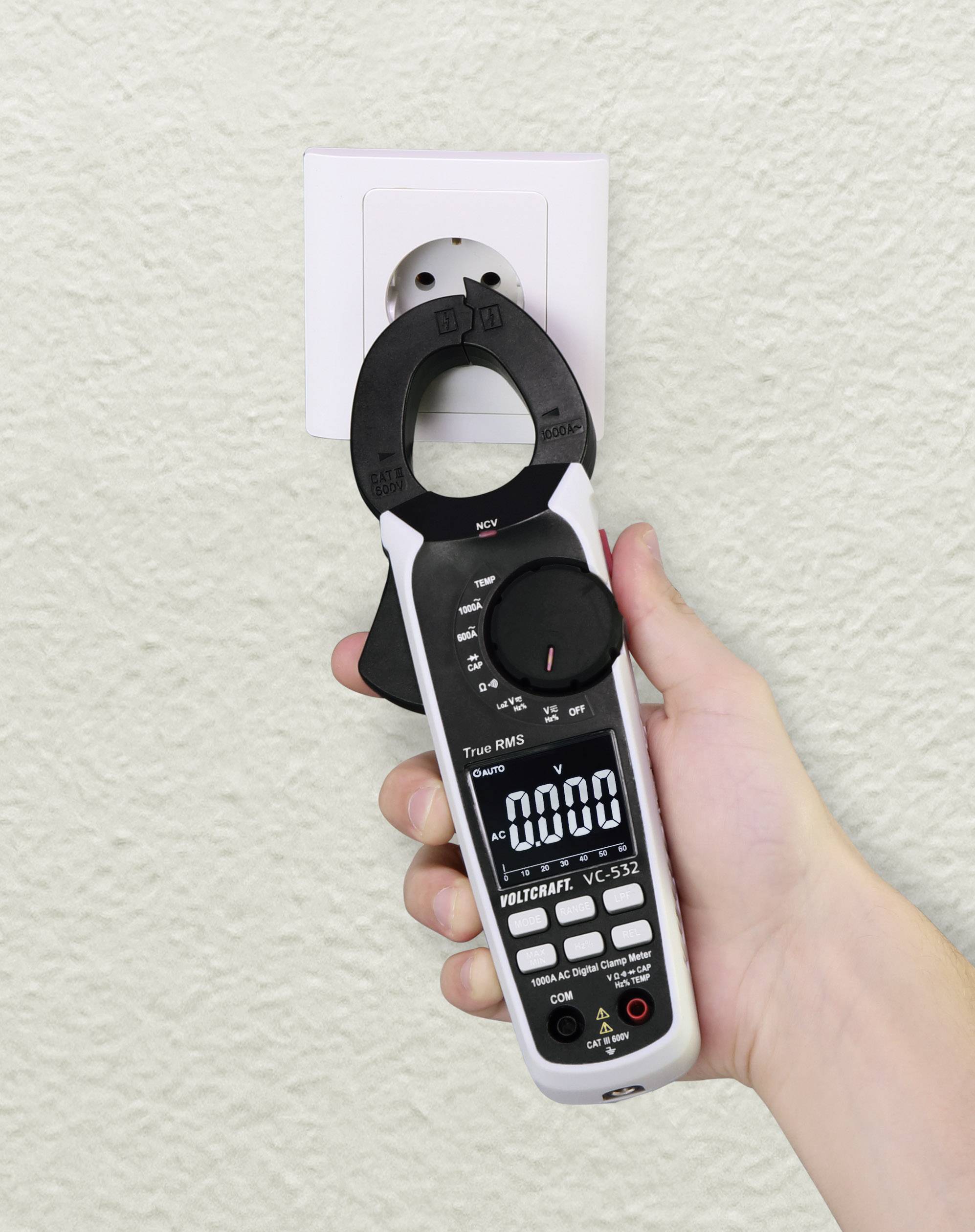 Hand houdt een digitale multimeter vast die op een stopcontact is gericht. Het display toont nul, wat aangeeft dat er geen stroomstroom wordt gedetecteerd.