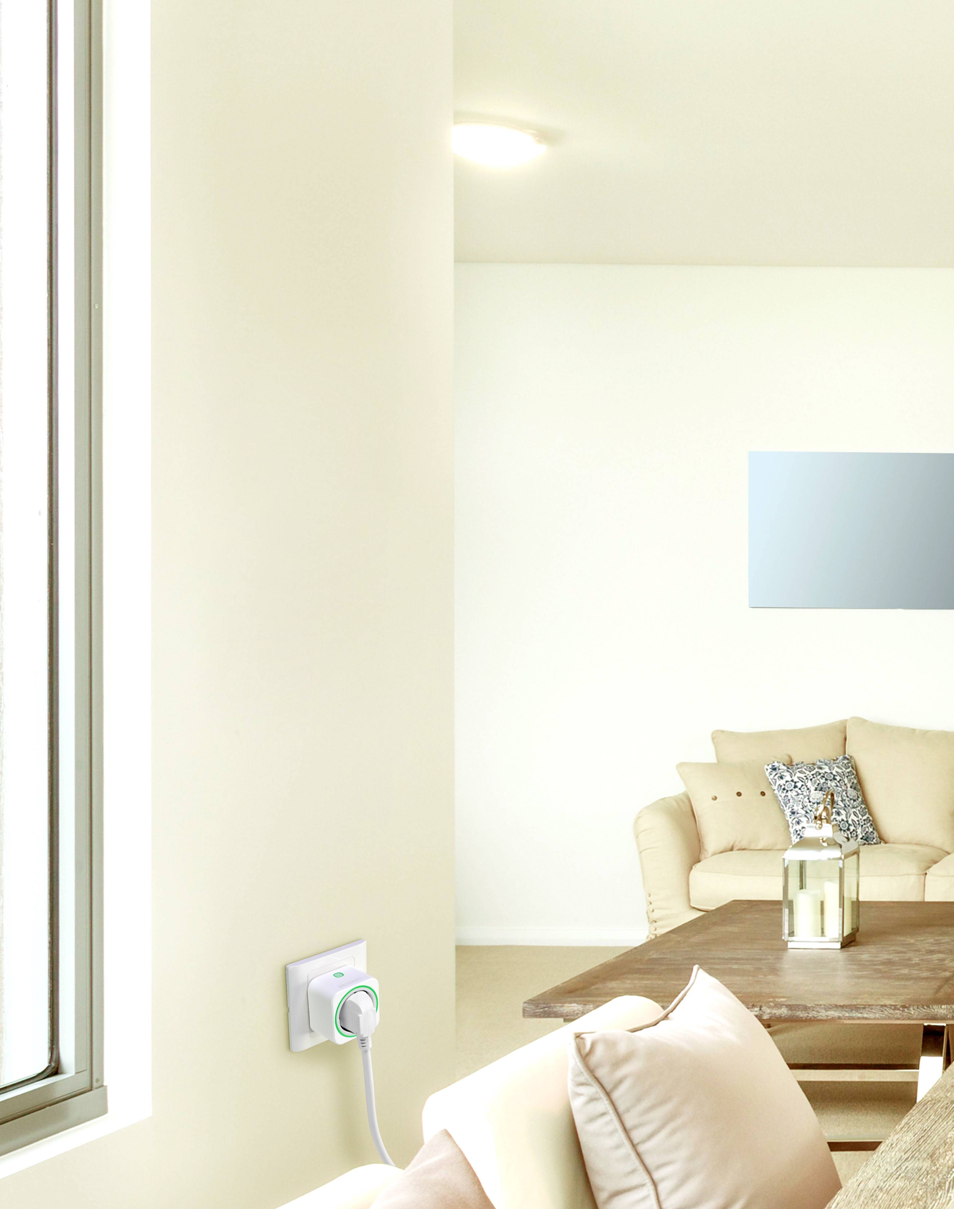 Lichte woonkamer met een beige bank, houten tafel en decoratieve kussens. Aan de muur een moderne stekkerdoos. Grote ramen laten licht binnenstromen.