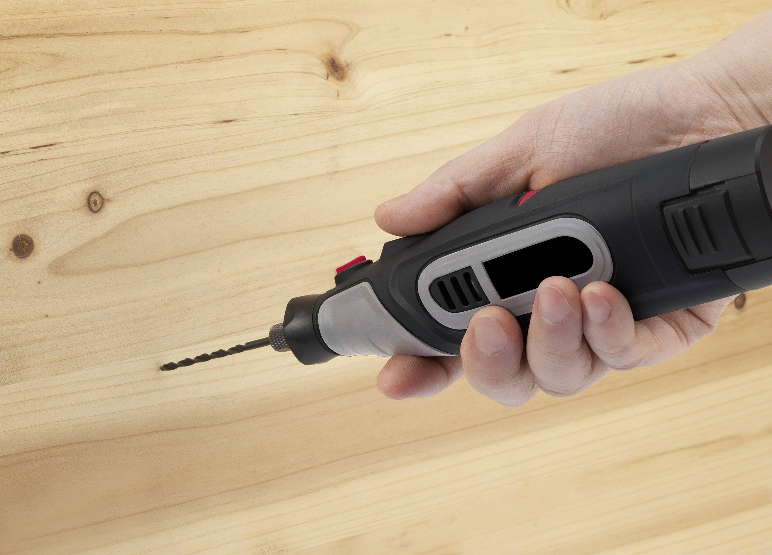 Een hand houdt een elektrische boormachine die op een houten oppervlak is gericht.