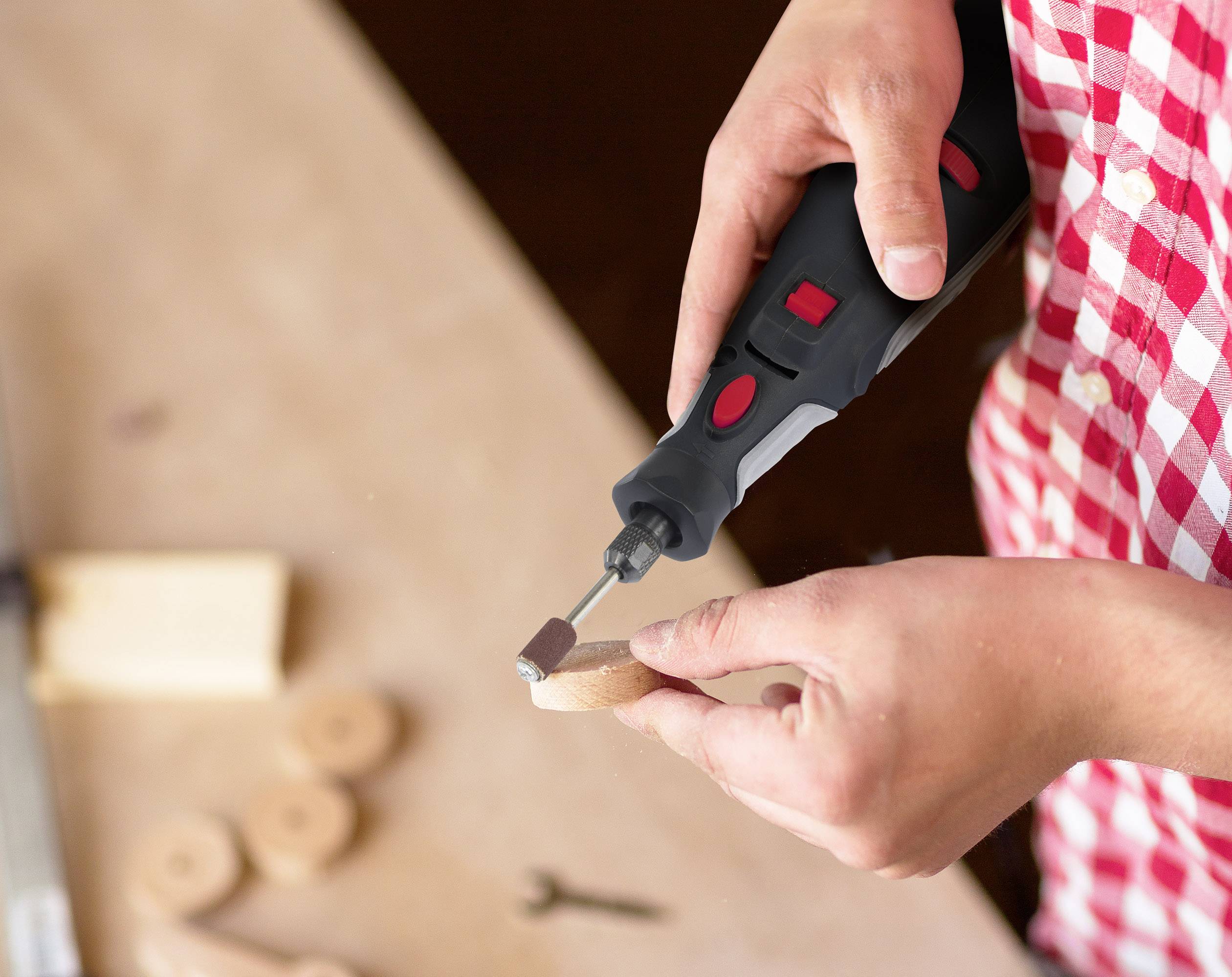 Een persoon bewerkt een rond houten stuk met een rood-zwarte elektrische slijpmachine op een tafel.