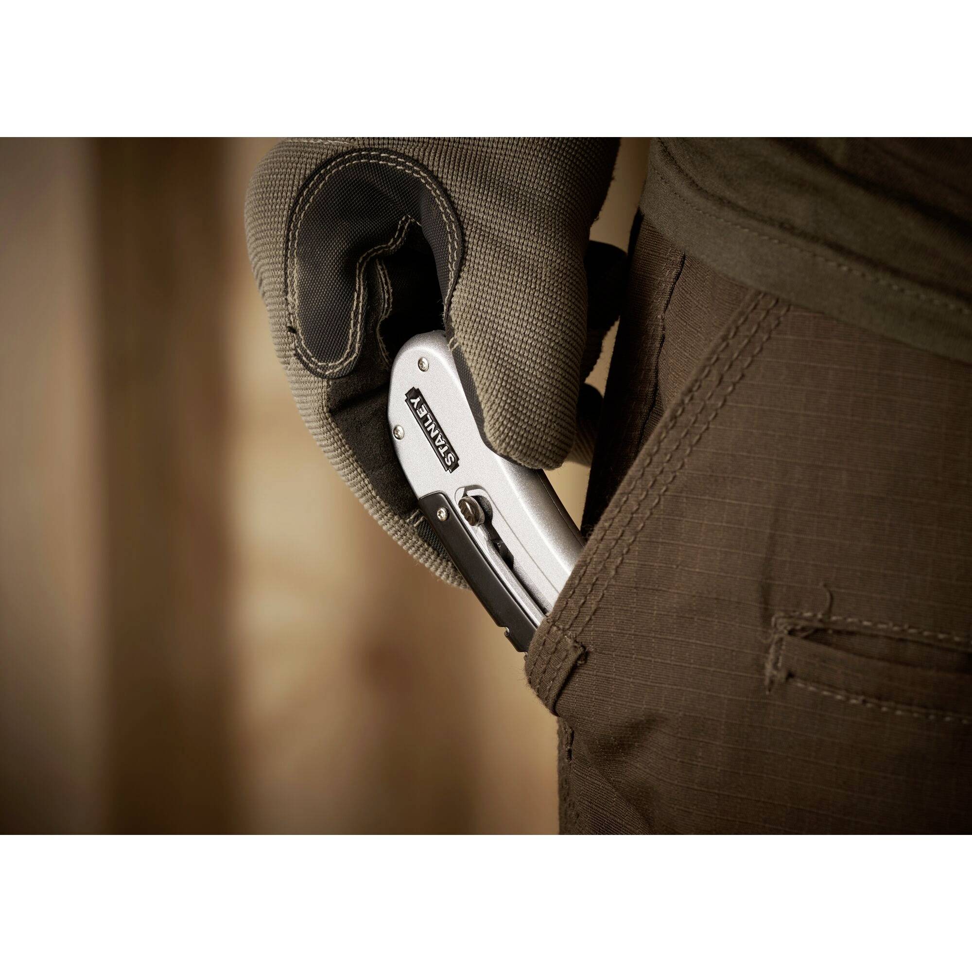 Een gehandschoende hand steekt een opvouwbaar multifunctioneel gereedschap in de broekzak.