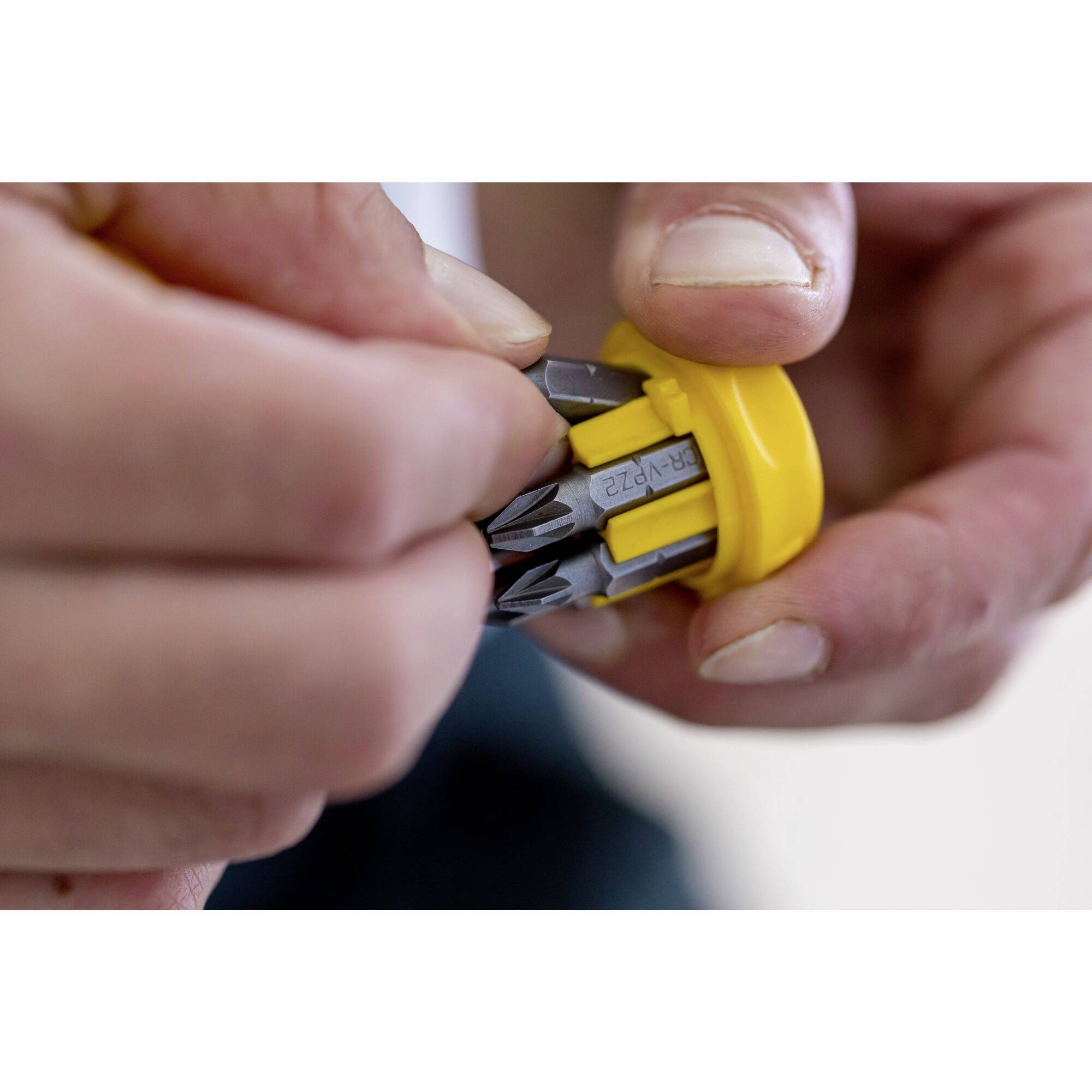 Een persoon houdt een gele schroevendraaierbithouder vast die meerdere bits bevat. De focus ligt op het wisselen van gereedschap.