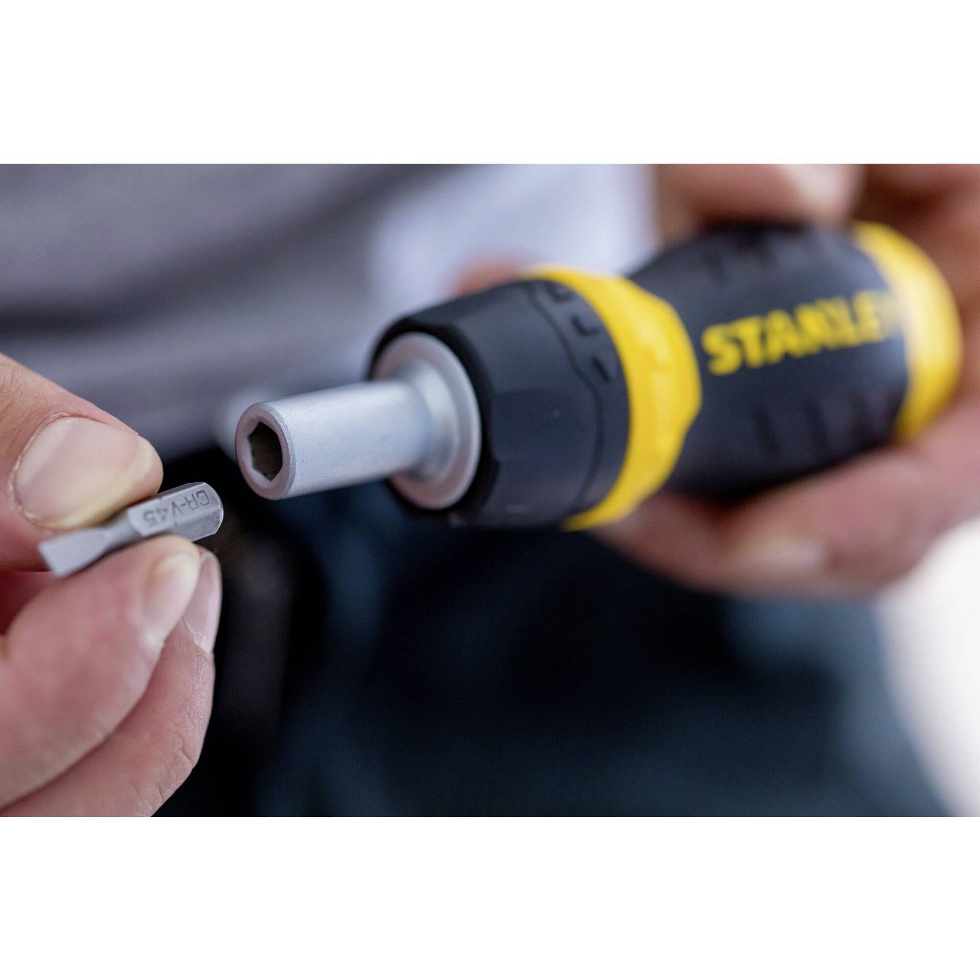 Een hand houdt een G7-auto-schroeropzetstuk vast om het in een gele en zwarte accuschroevendraaier te plaatsen.