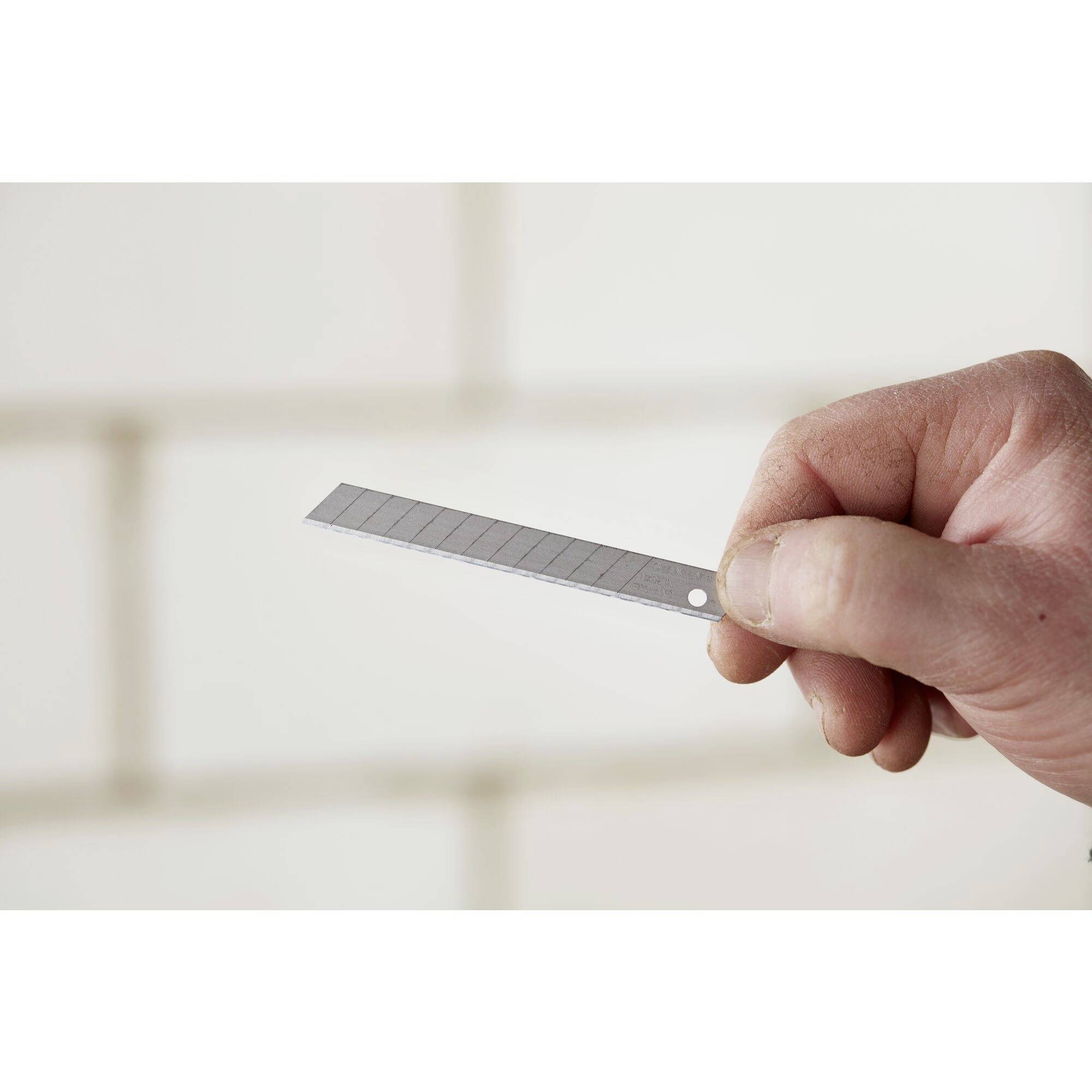 Een hand houdt een stanleymes in de lucht, klaar om te snijden of te knutselen. De achtergrond is wazig.