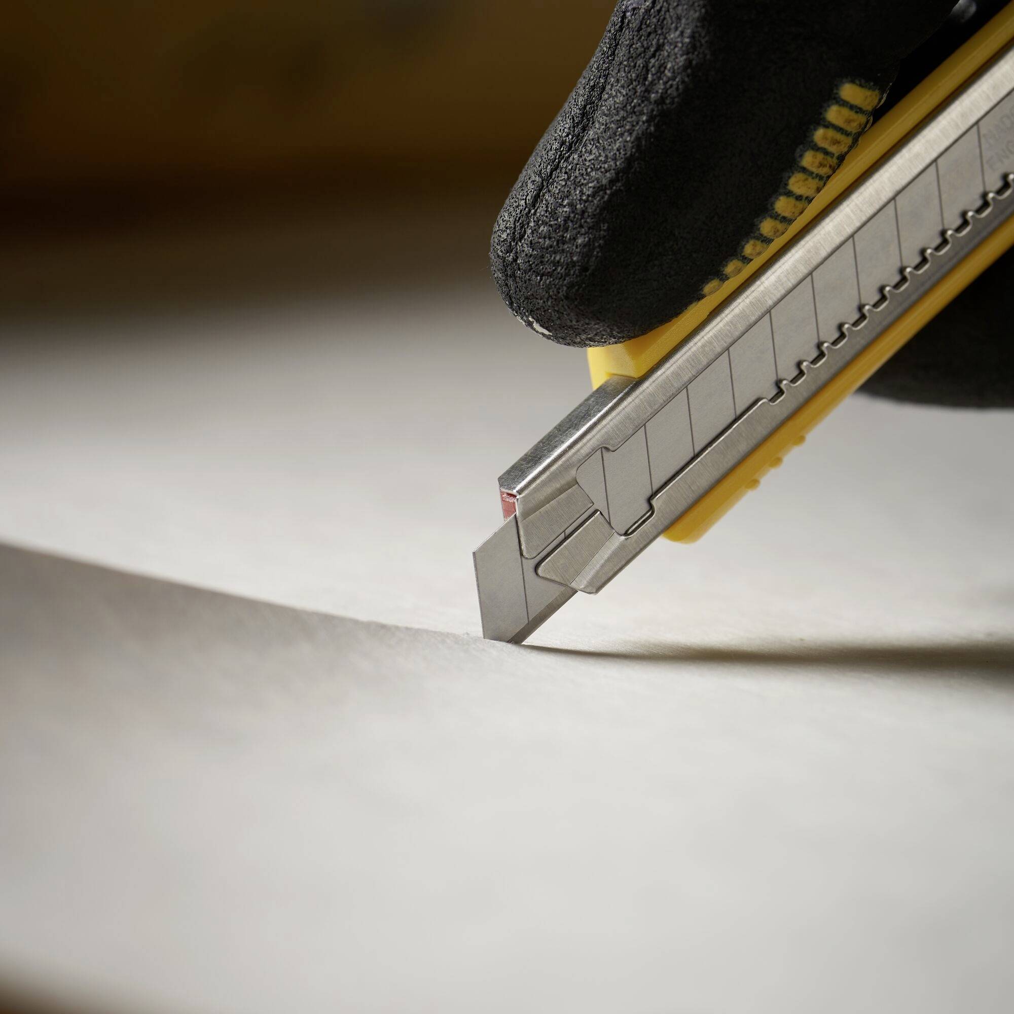 Een stanleymes in een zwarte handschoen snijdt een vel papier op een tafel.