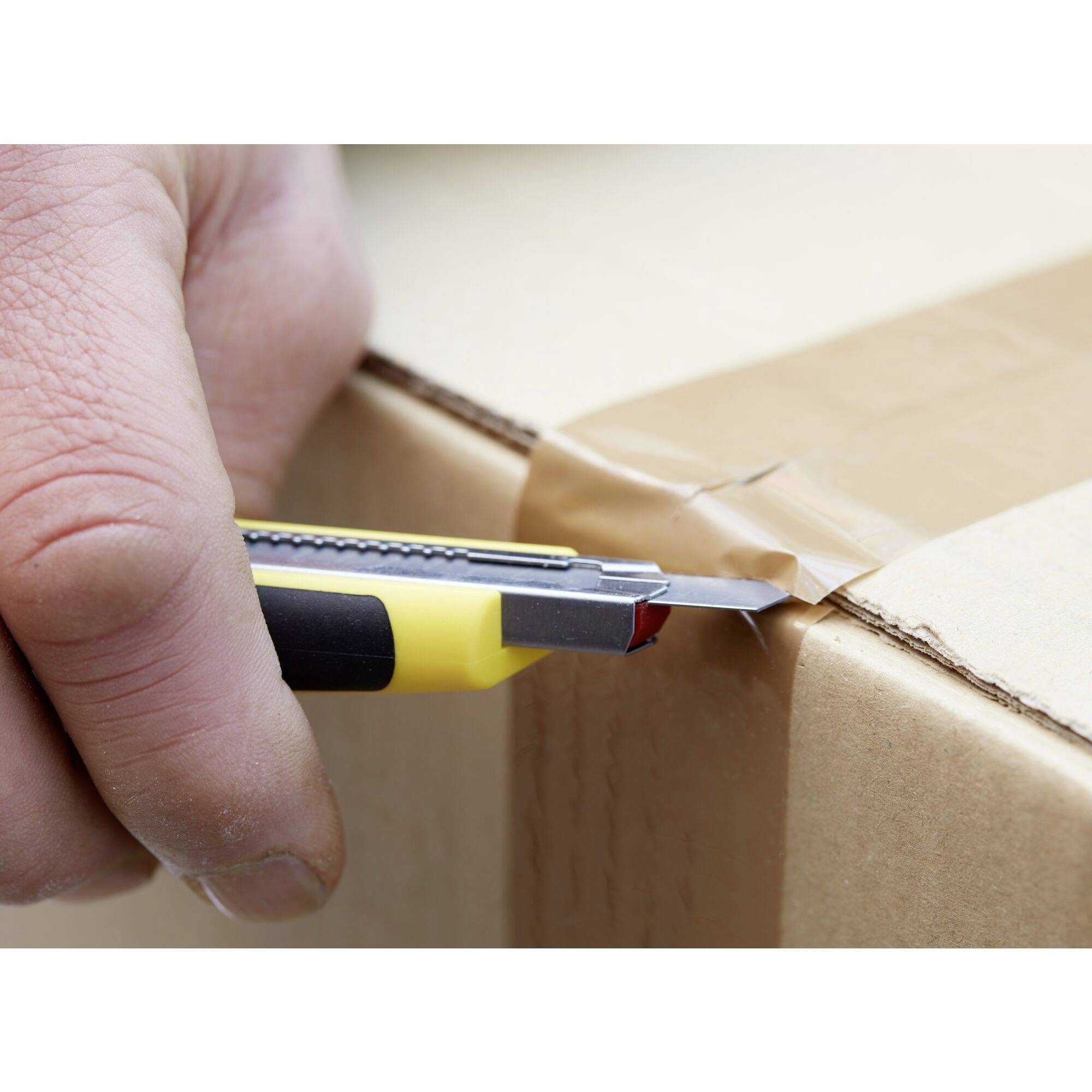 Een hand snijdt plakband door met een geel stanleymes op een kartonnen doos.