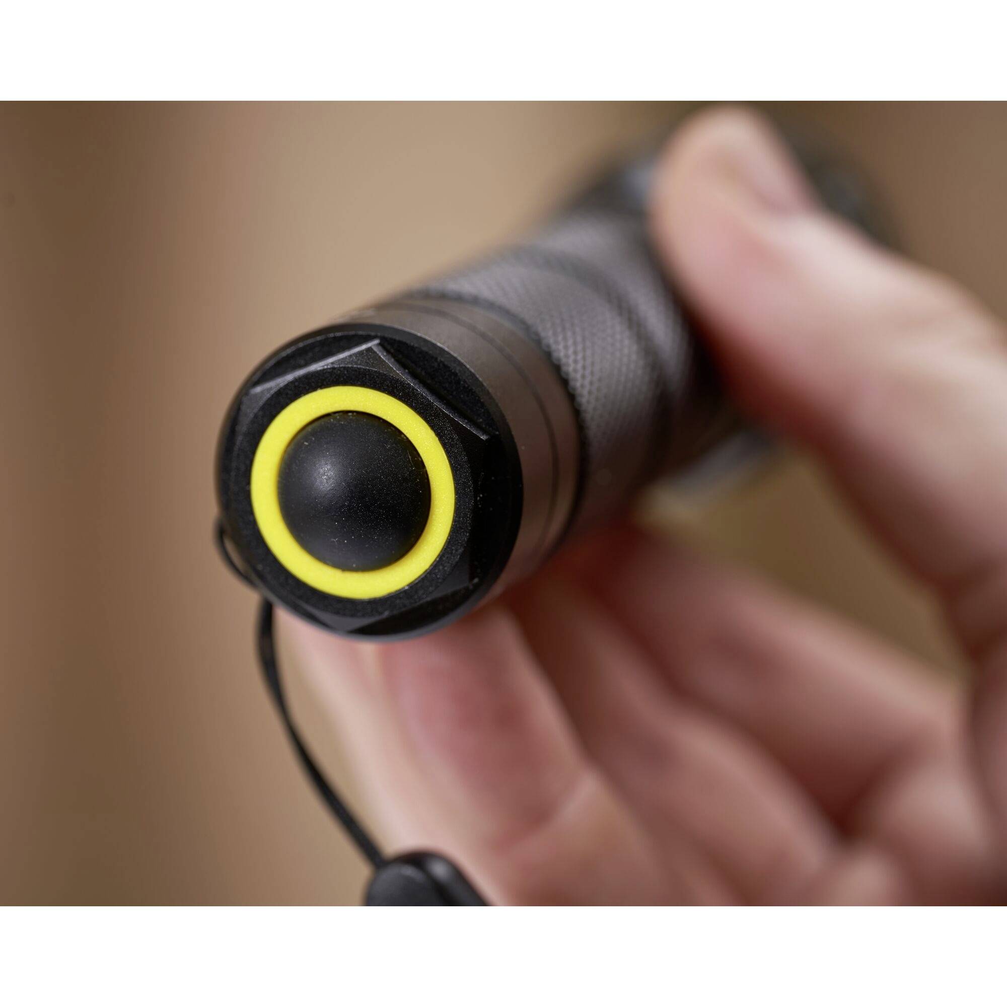 Duim drukt op de gele knop van een zwarte zaklamp. Focus op de antislip handgreep en de hand die het apparaat vasthoudt.
