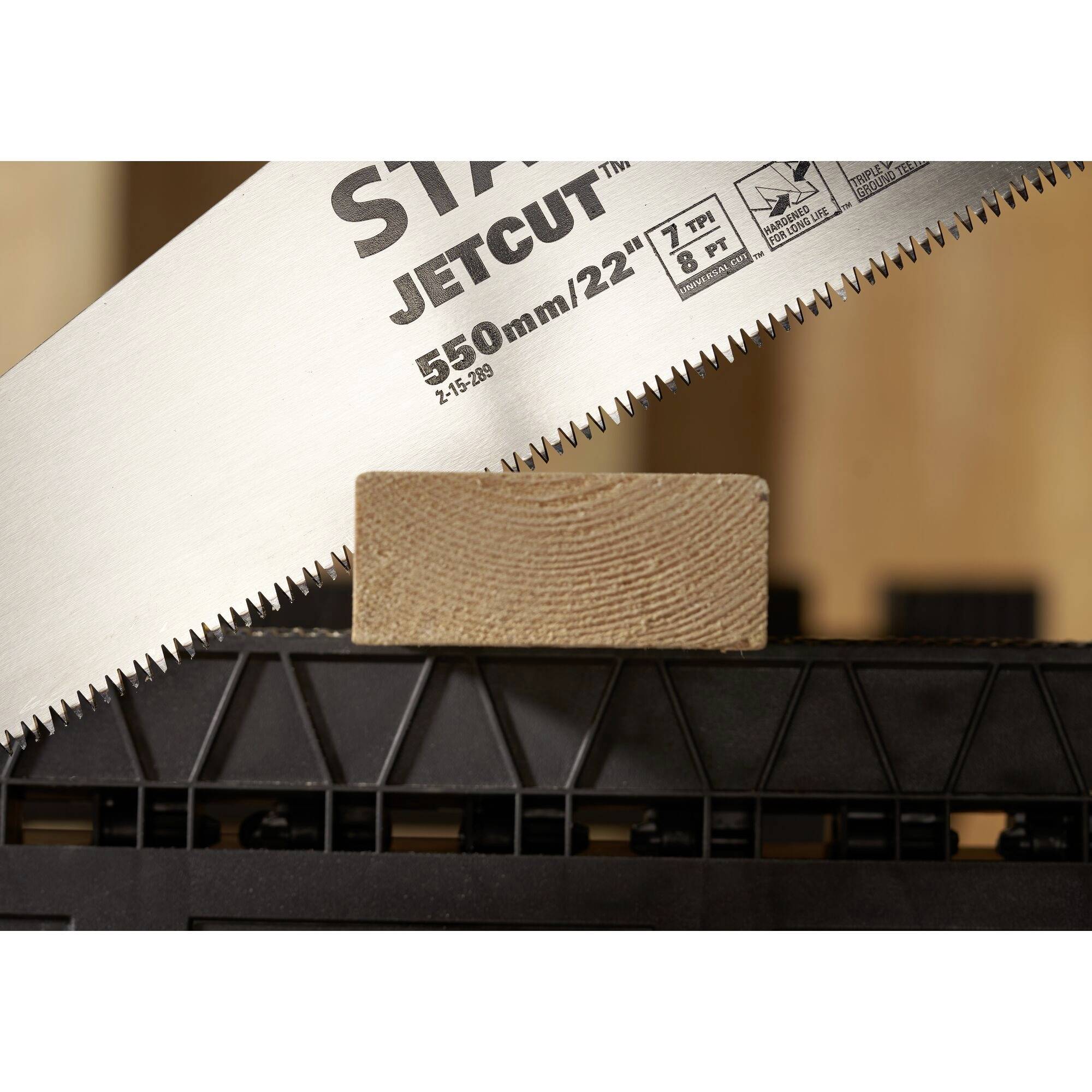 Een handzaag snijdt een stuk hout op een werkbank. De zaag vertoont de opdruk 'JETCUT 550mm/22" 7 tpi'.
