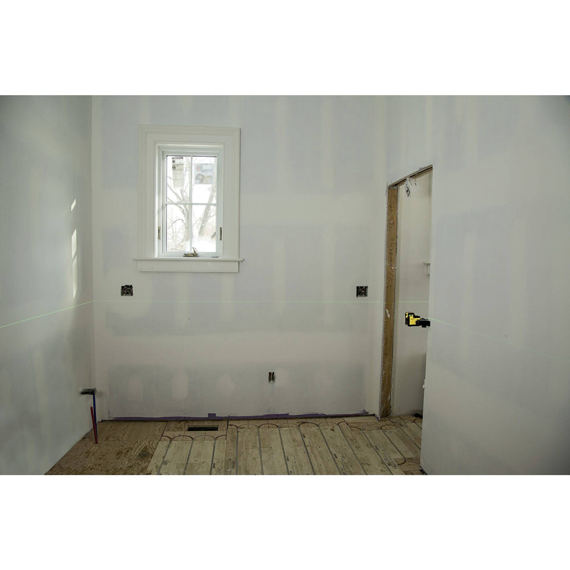 Een lege ruimte met een houten vloer, witgeschilderde muren, een raam en een halfafgewerkte deuropening. De ruimte verkeert in aanbouw.