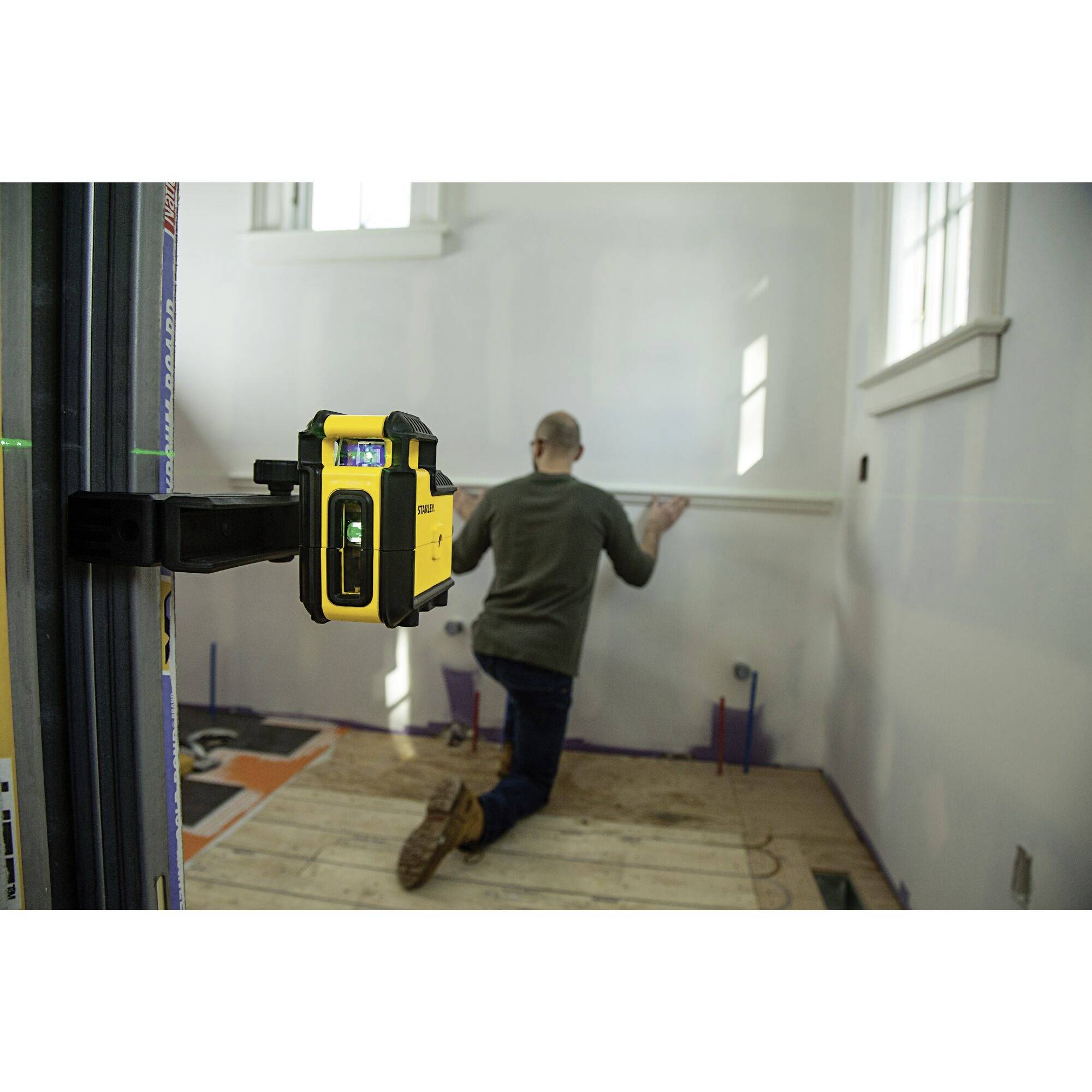 Een man bevestigt een rail aan de muur met een geel lasergereedschap in een witte ruimte.