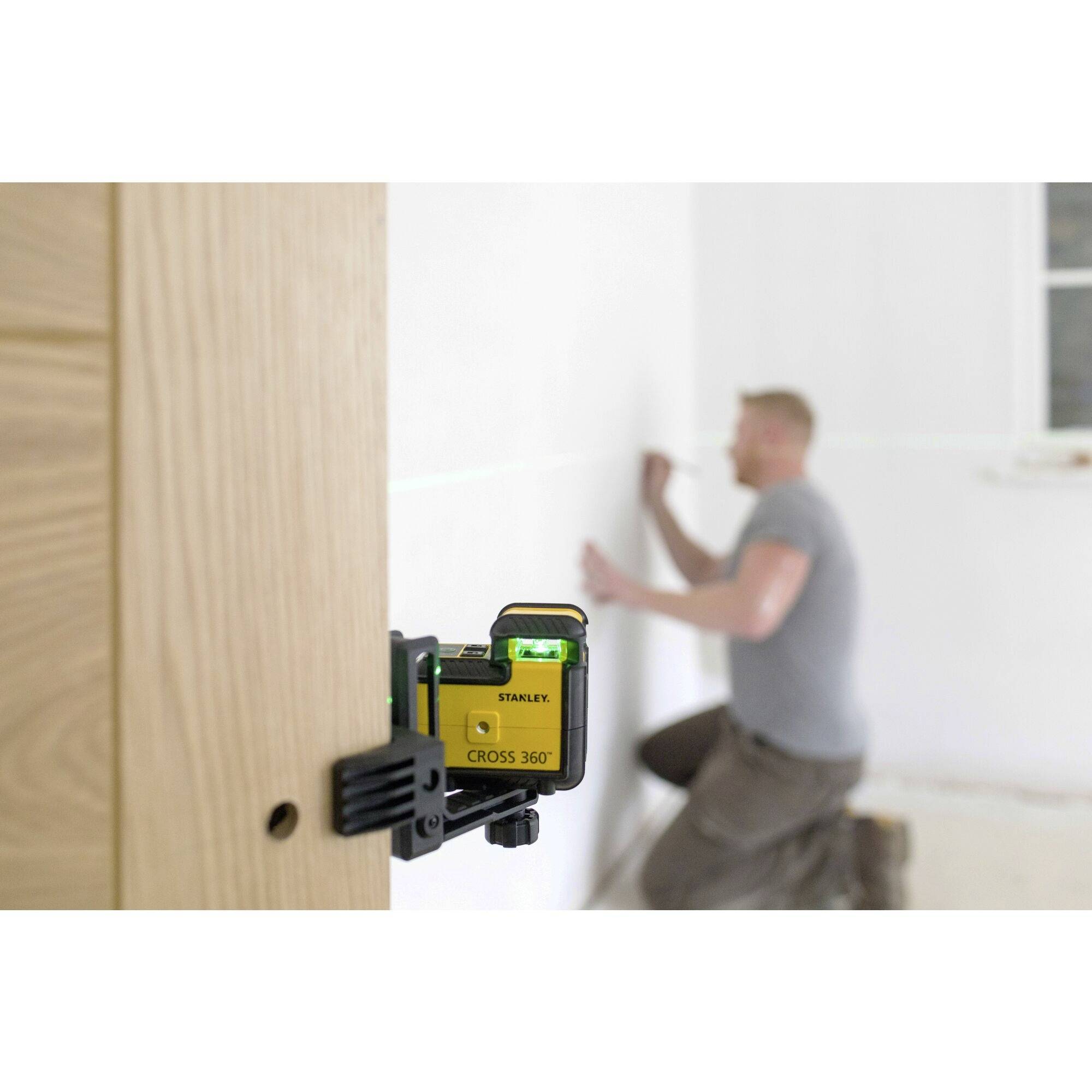 Een man richt een lijn aan de muur met behulp van een laserwerktuig op de voorgrond, ter voorbereiding van muurwerkzaamheden.