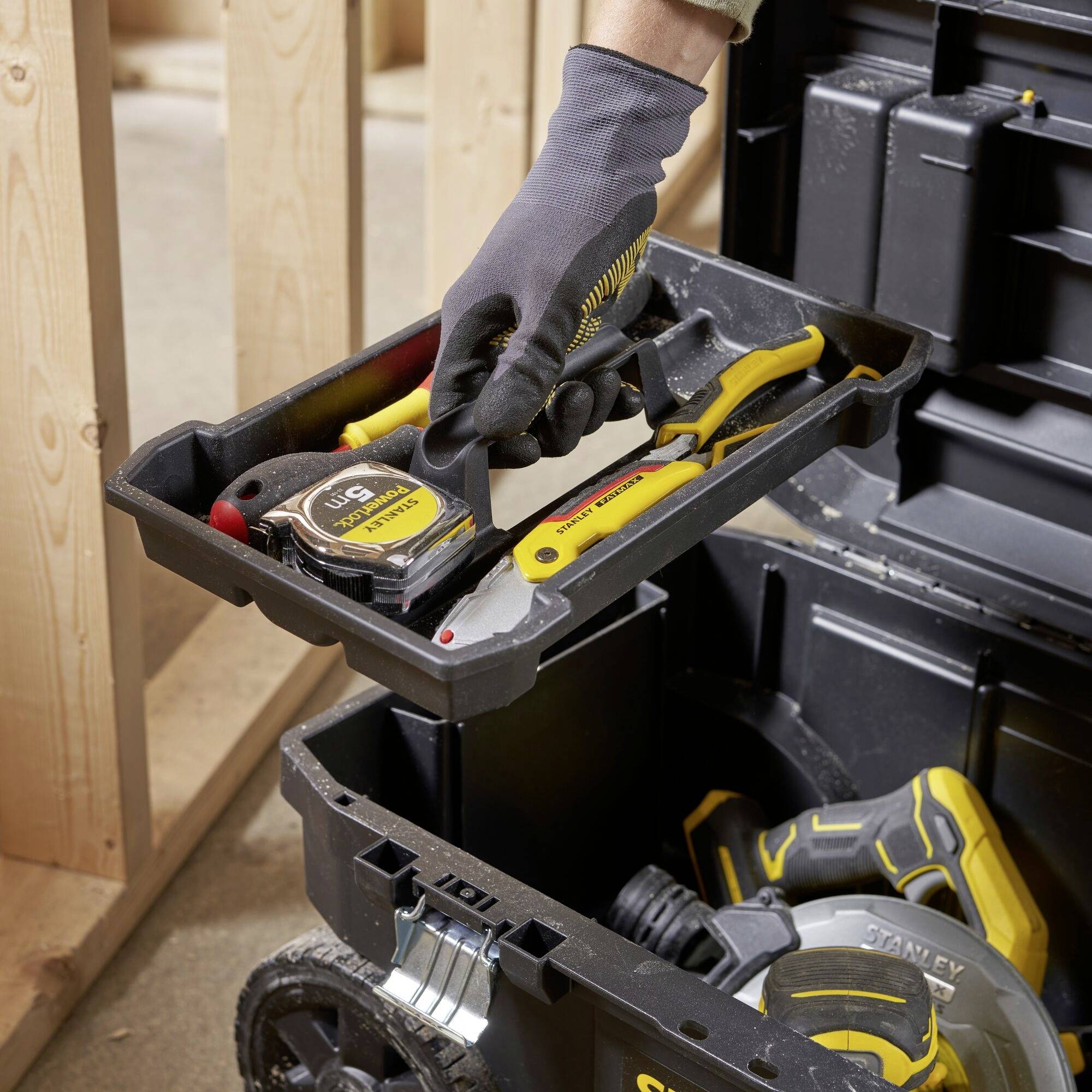 Een persoon die in een houtatelier werkt, gebruikt een meetlint en haalt het uit een gereedschapskist met verschillende gereedschappen.