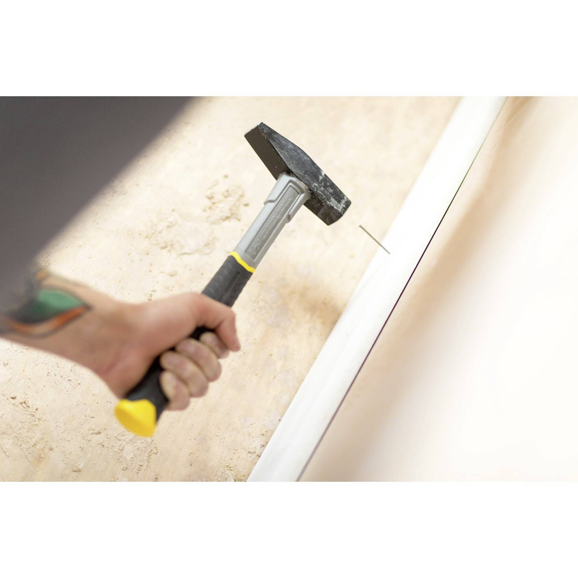 Een hand houdt een hamer vast en slaat een spijker in de muur. De afbeelding toont een activiteit van doe-het-zelven of renovatie.