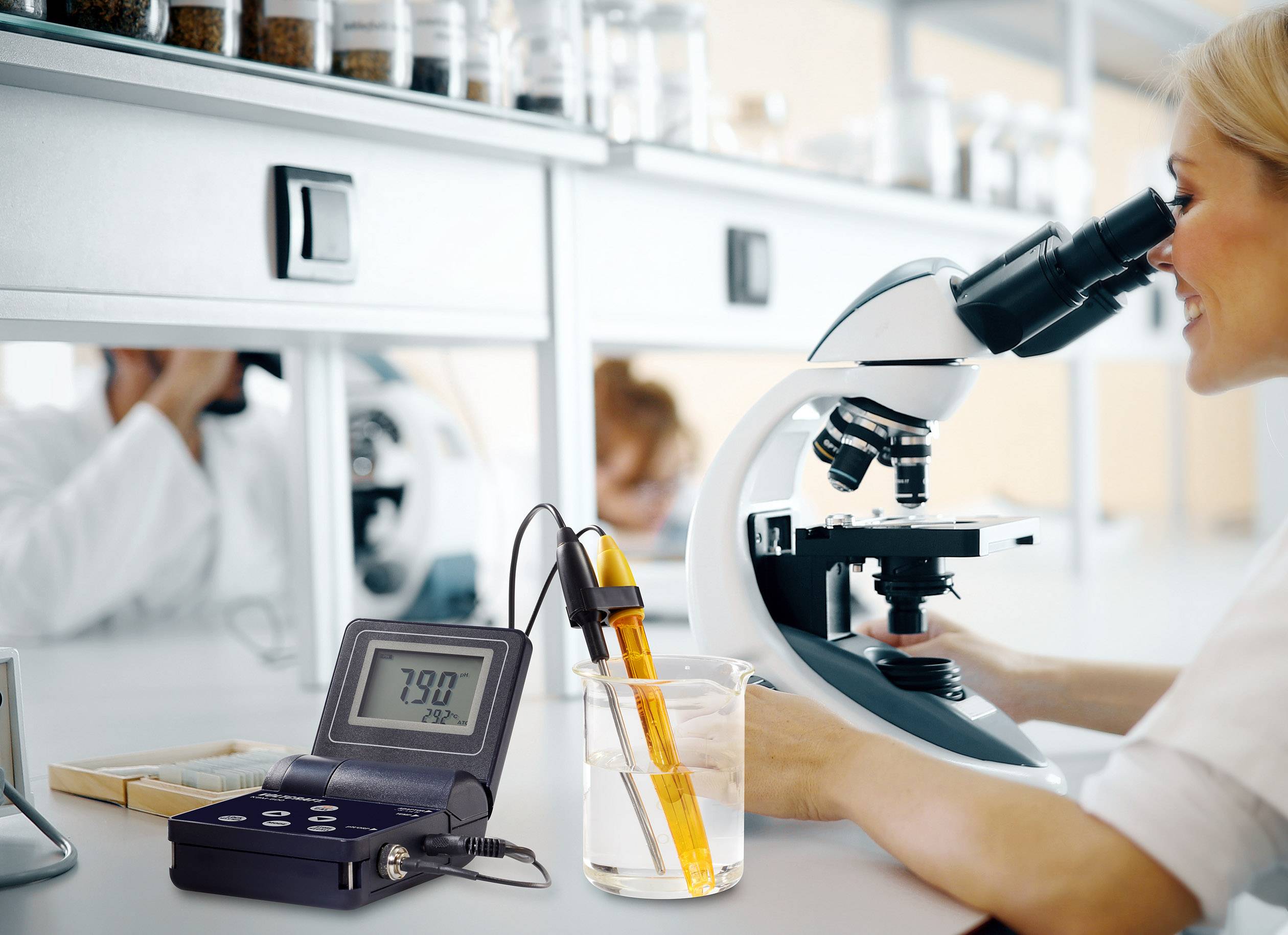Een wetenschapster kijkt door een microscoop, terwijl een digitaal meetapparaat op de voorgrond de pH-waarde van een vloeistof aangeeft.