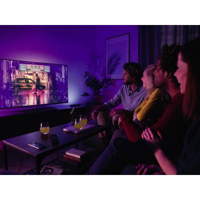 Een groep van vier personen zit op een bank samen een film te kijken op een grote televisie in een donkere kamer.