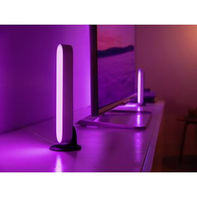 Twee slanke, verticaal geplaatste LED-lampen schijnen in intens paars naast een beeldscherm op een modern bureau.