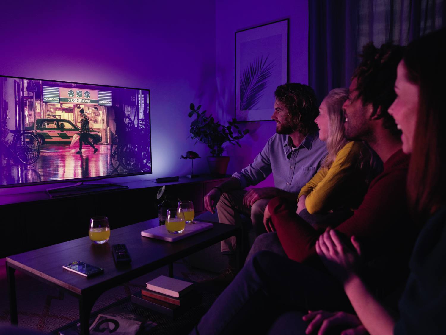 Vier personen zitten gezellig in een woonkamer en kijken samen een film op een grote televisie.
