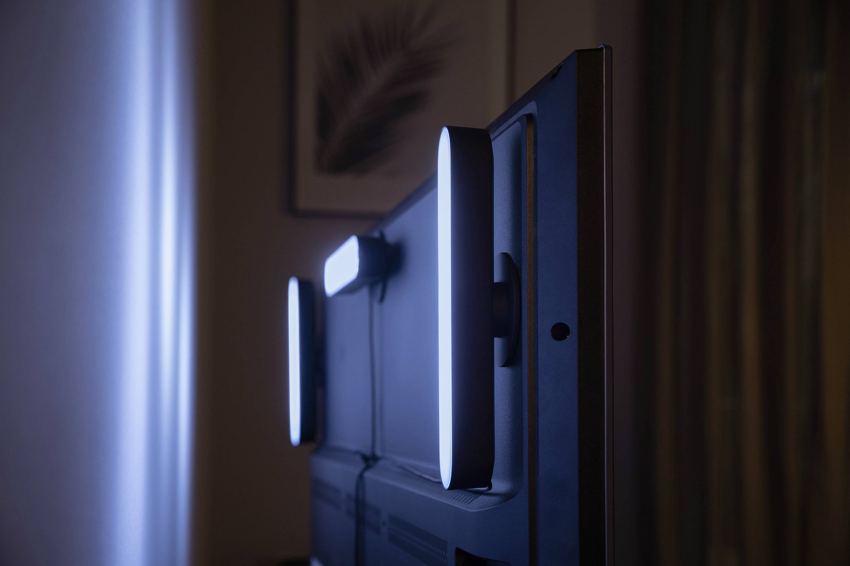 Zijaanzicht van een monitor met drie oplichtende LED-lampjes aan de achterkant, in een donkere ruimte met sfeervolle verlichting.