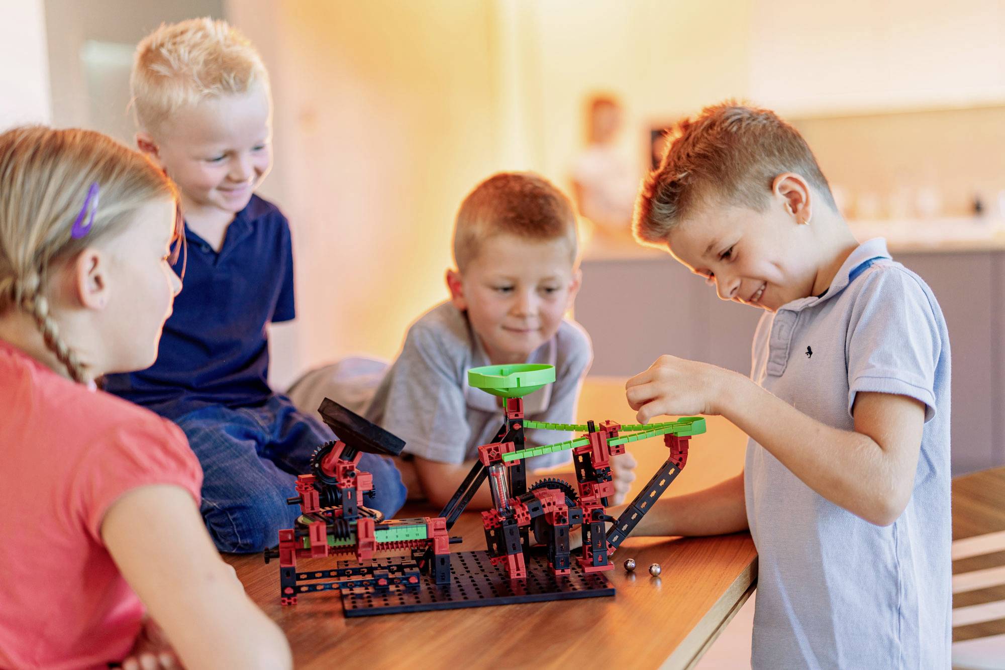 Kinderen spelen enthousiast met een constructiedoos vol kleurrijke bouwstenen aan een tafel. Ze zijn geconcentreerd bezig met hun gezamenlijke project.