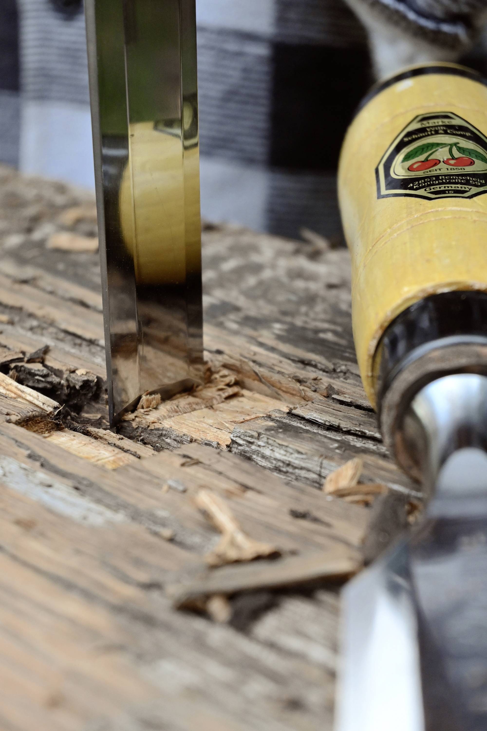 Houtbewerking: Close-up van een steekbeitel die een stuk hout binnendringt. Houtkrullen en een scherp mes zijn zichtbaar.