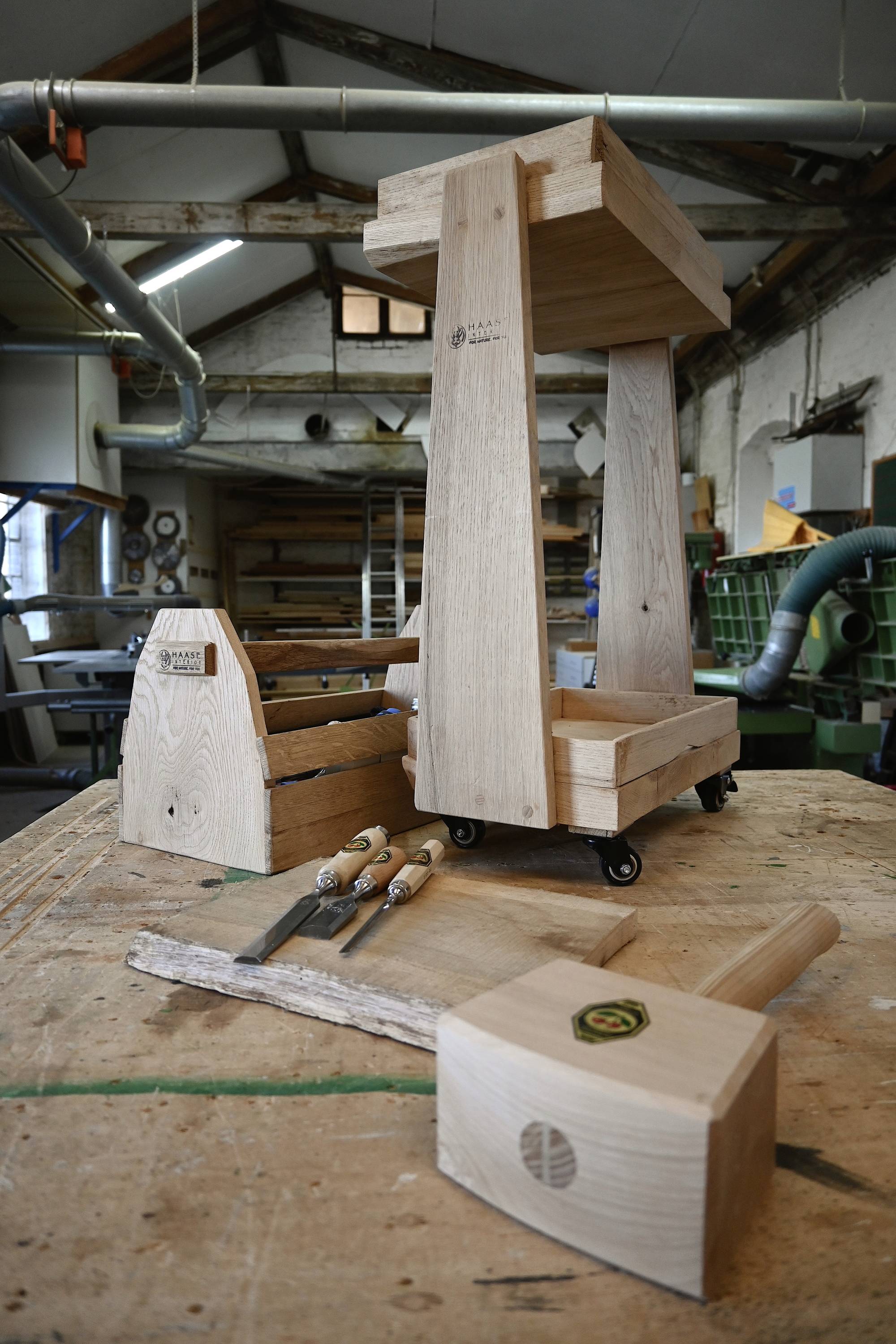 Een werkplaats met houten gereedschappen, inclusief een mobiele werkbank op wielen, een houten hamer en snijgereedschappen.