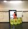 Een arbeider in een oranje veiligheidshesje veegt een reclamedisplay schoon in een metrostation. Om hem heen staan afzettingen.