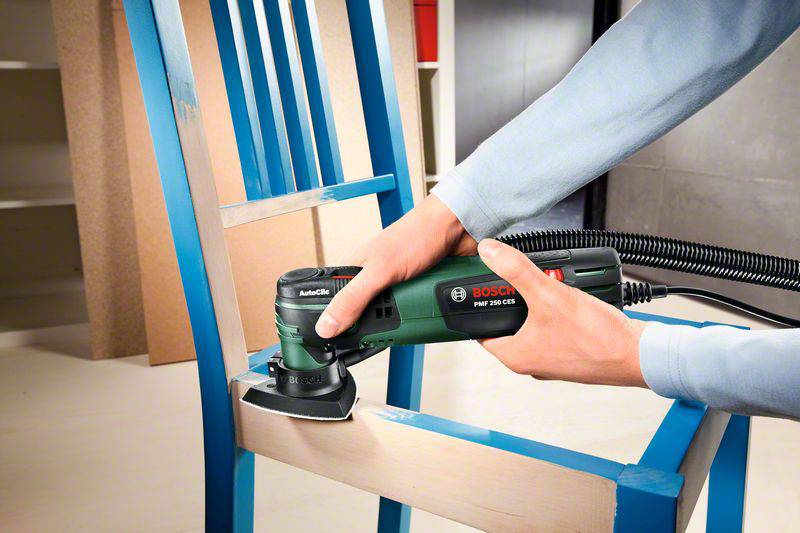 Een persoon schuurt met een Bosch-gereedschap de zitting van een blauwe houten stoel om deze te renoveren of glad te maken.