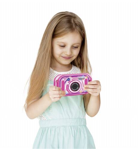 Meisje met lang haar houdt een roze speelgoed camera vast en glimlacht terwijl ze naar beneden kijkt.