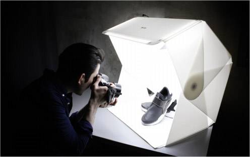 Een fotograaf maakt een foto van een zwarte schoen in een goed verlichte, witte fotokubus.
