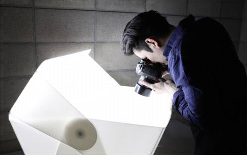 Een persoon fotografeert een architectonisch model met een camera. De scène is helder verlicht, de omgeving oogt professioneel.